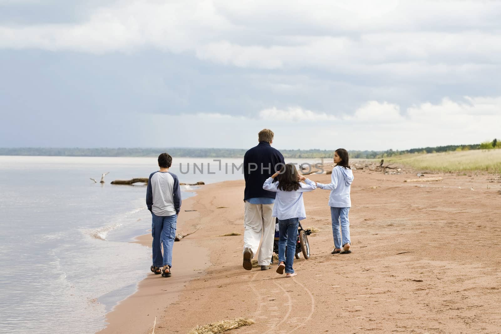 Father and children strolling along the deserted lake shore on sunny day