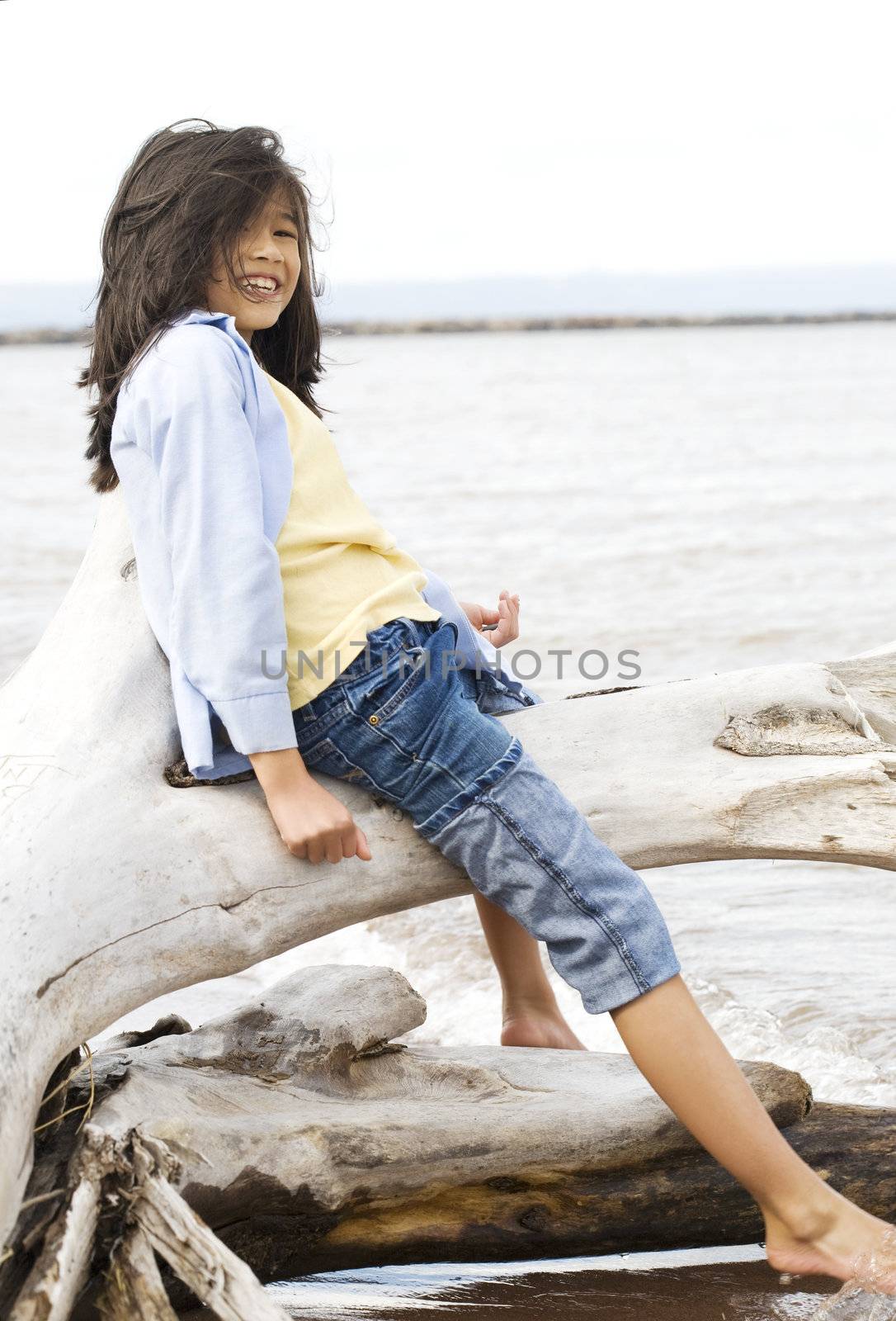 Little girl playing on fallen tree by lake shore in summer