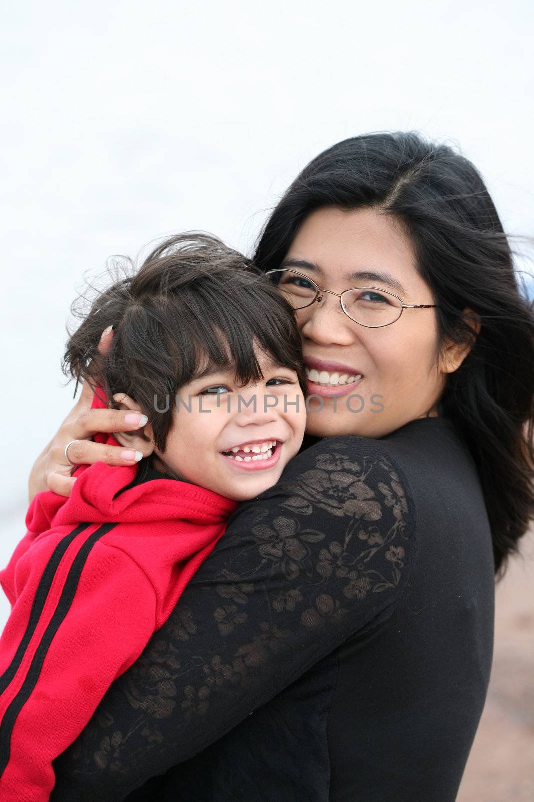 Asian mother holding her little toddler boy outdoors by beach