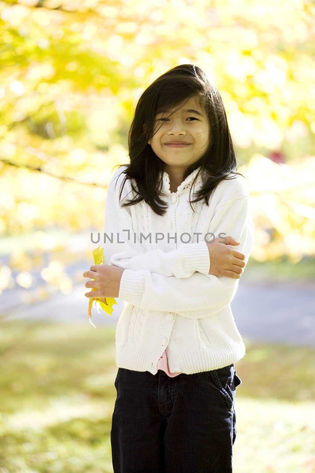 Little biracial asian girl standing amongst bright autumn leaves