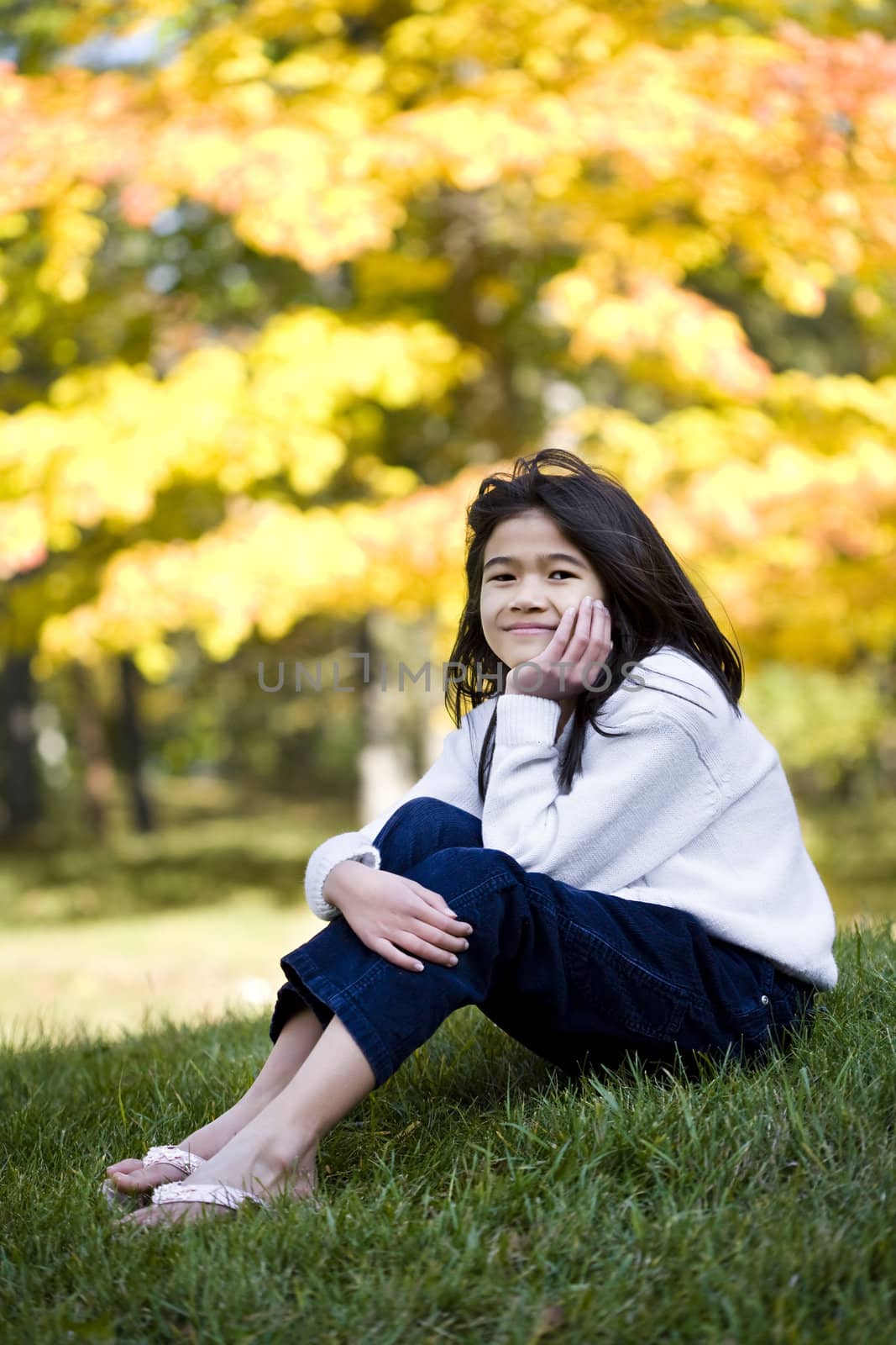 Girl sitting on grass with bright colorful autumn leaves in background