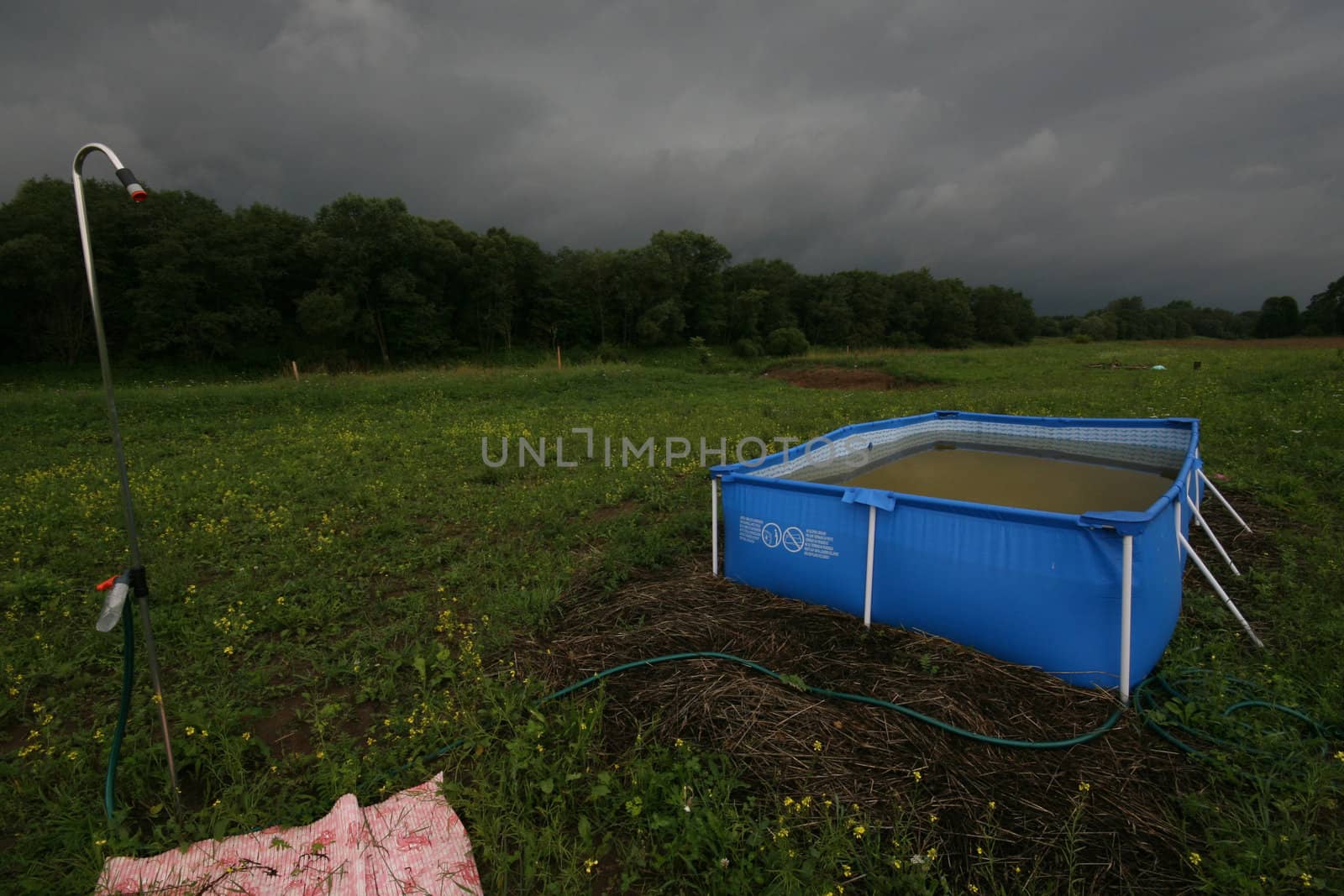 Swimming pool in the meadow at thunderstorm.
