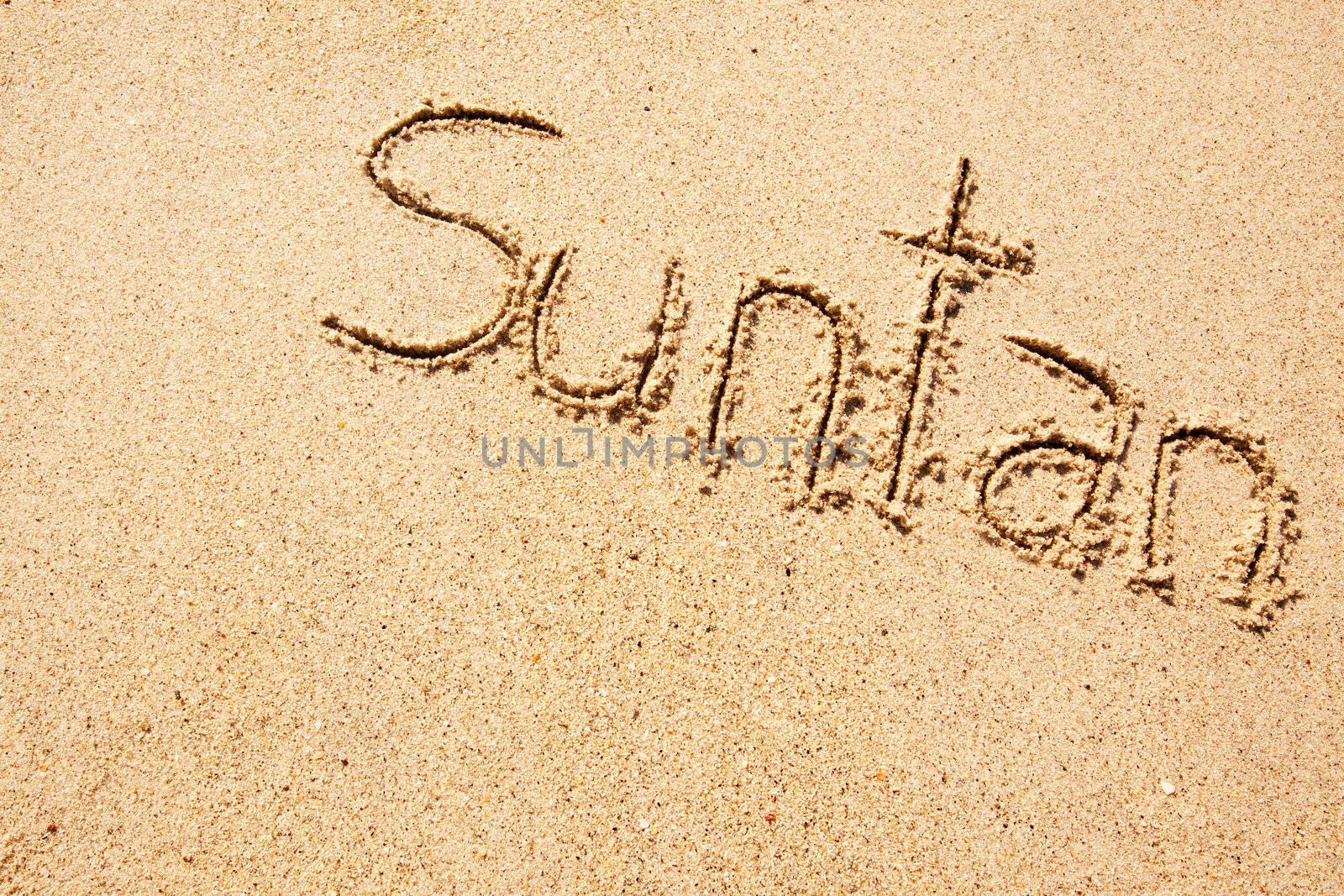 The word suntan written in the sand on a beach