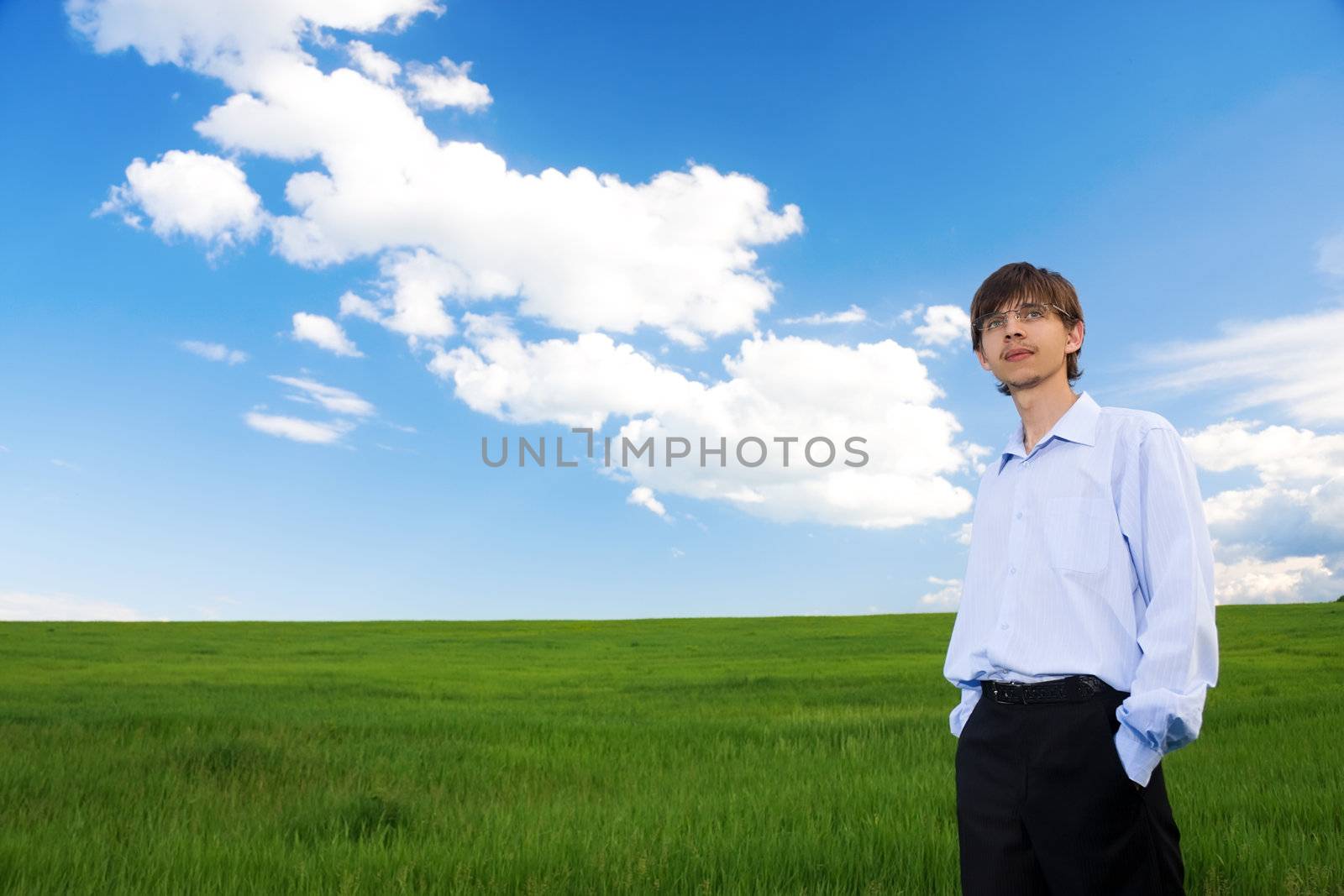 Successful businessman standing on green grassland under blue sky