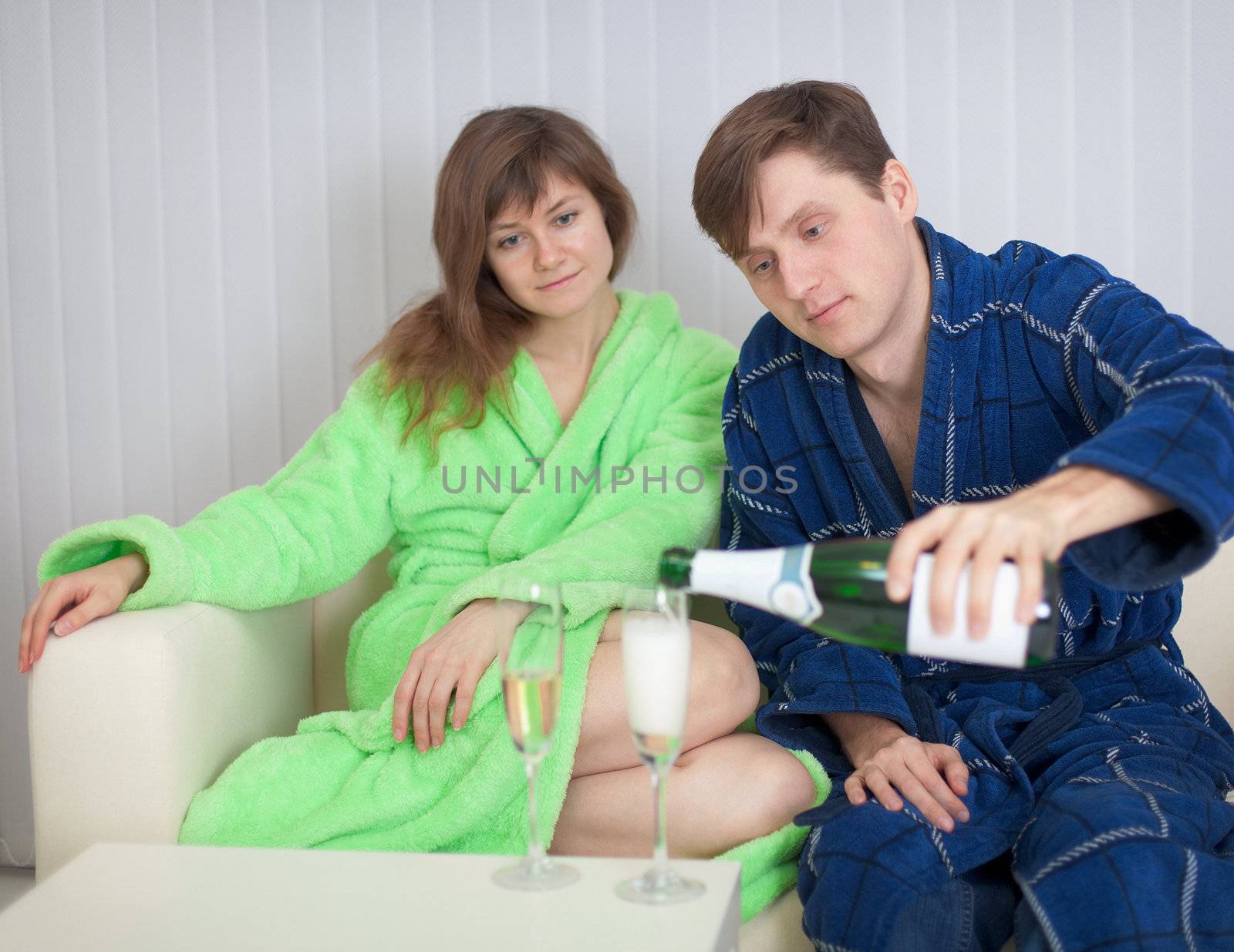 The young man in a dressing gown pours to the lady sparkling wine