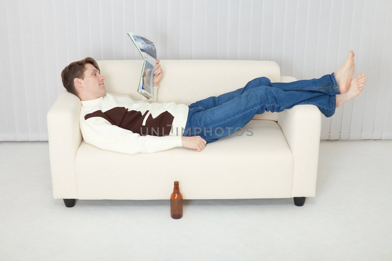 Person comfortably lie on a sofa with a beer and journal