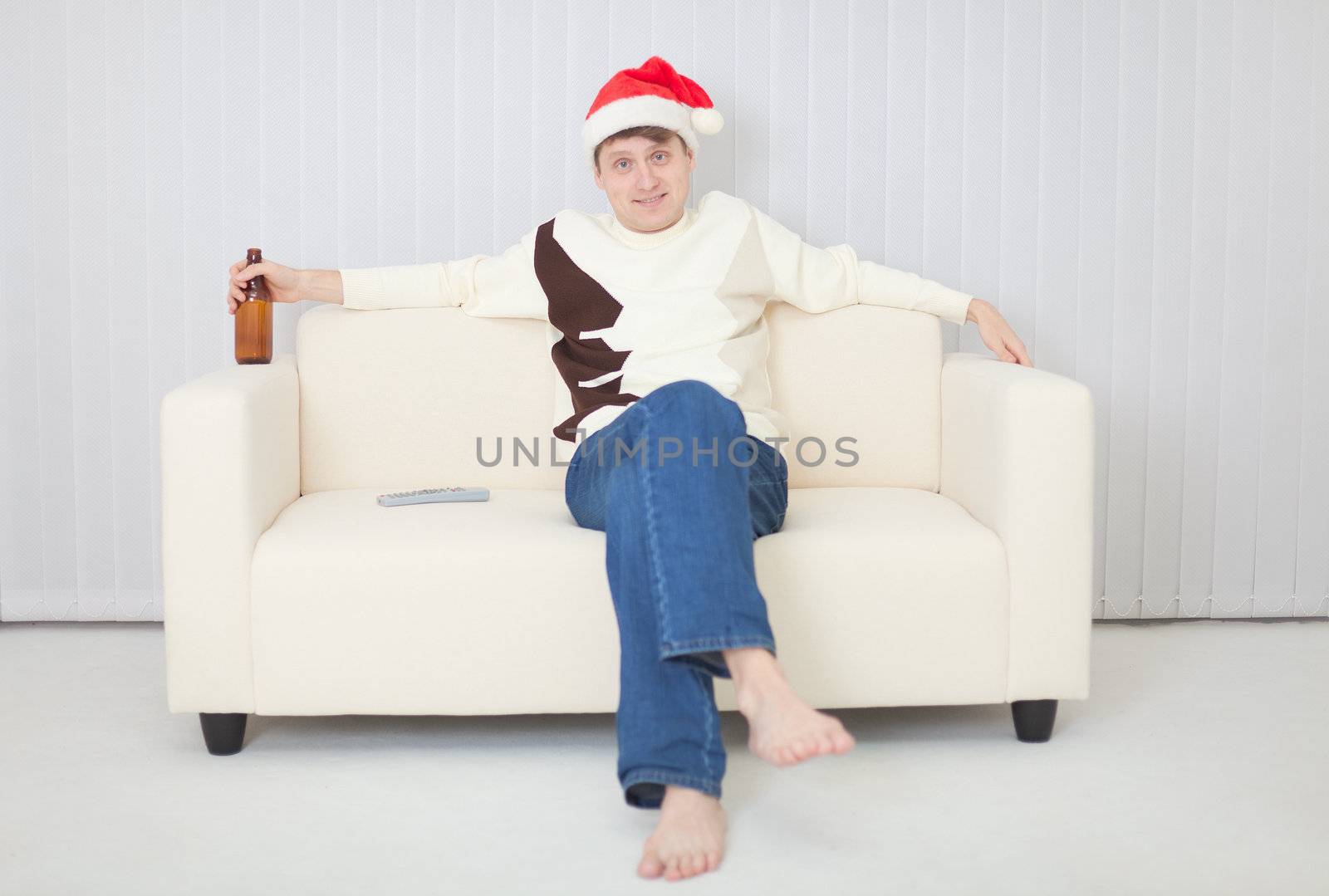 Person in a Christmas cap comfortably sits on sofa with beer by pzaxe