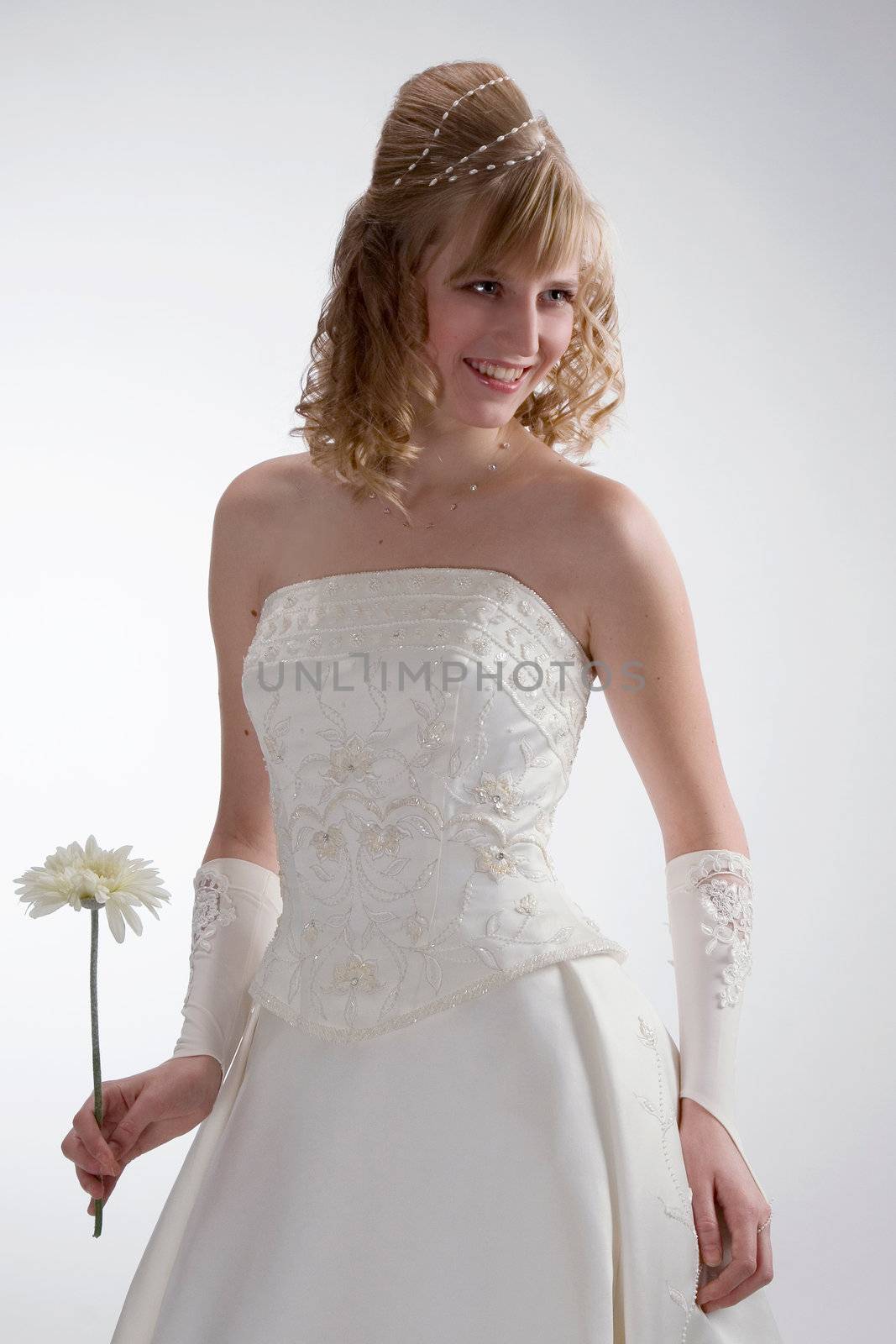 Beautiful bride in white dress with charming smile and white flower in her hand on the white background.
