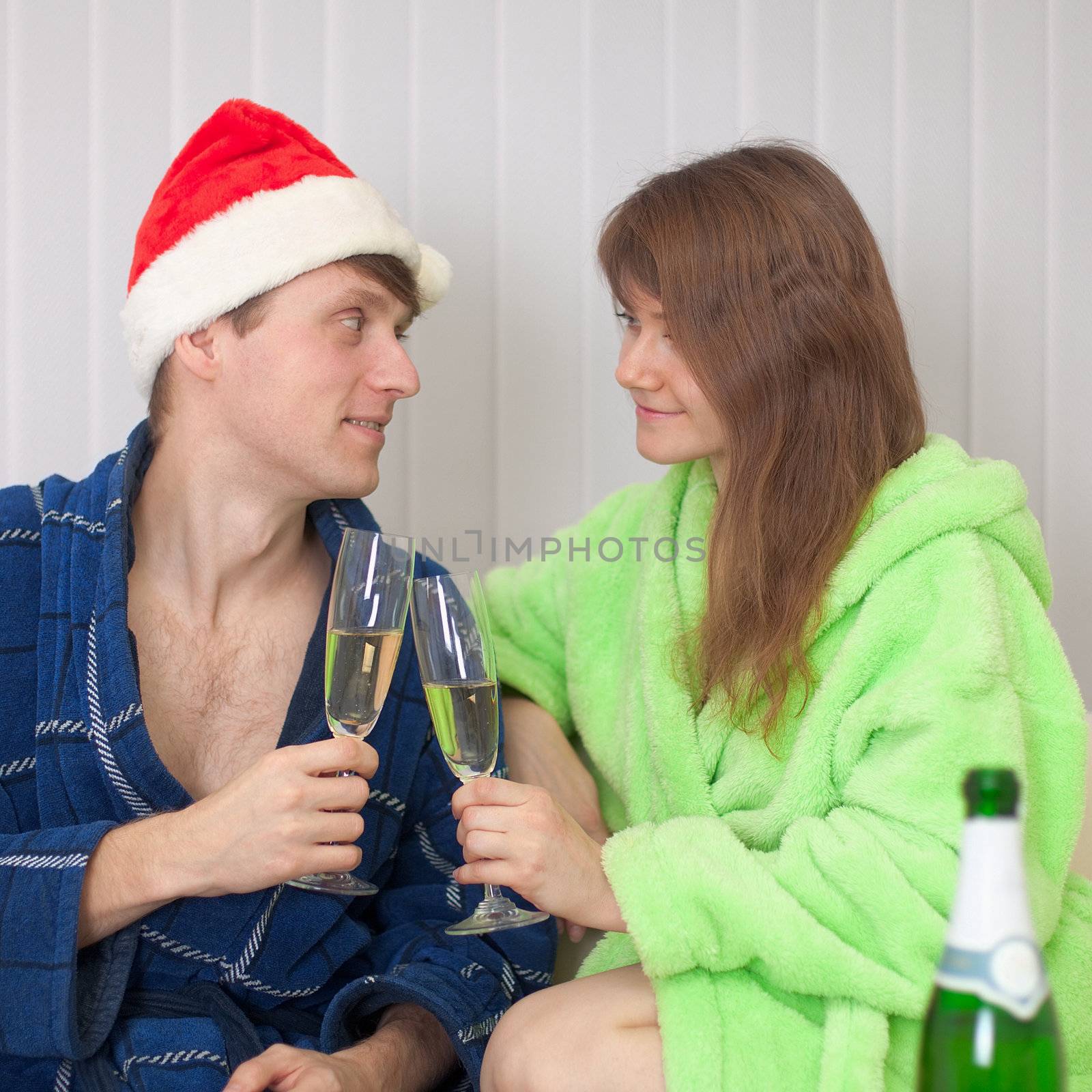 The young pair drinks champagne sitting on a sofa in dressing gowns