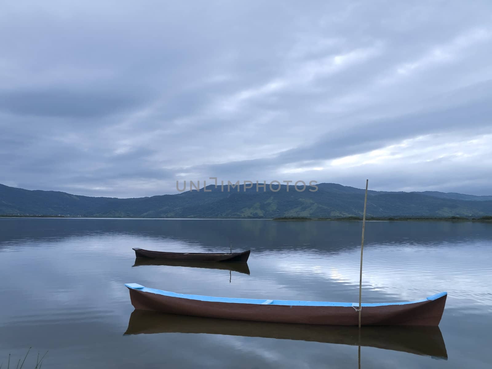 Two canoes tied on a quiet lake under a cloudy sky.