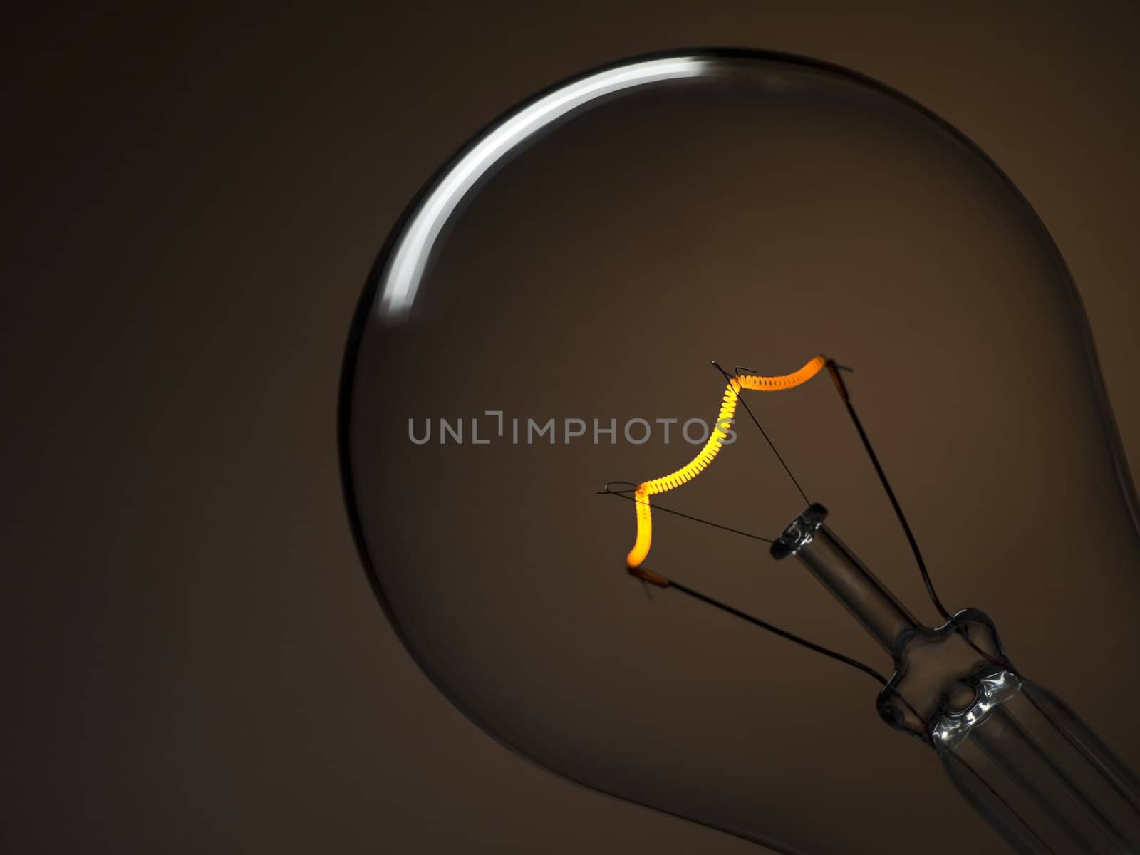 Close up on a turned on light bulb over a brown background.