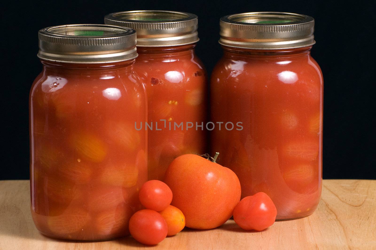 Three mason jars filled with canned tomatoes shot on a wooden board and isolated against a black background