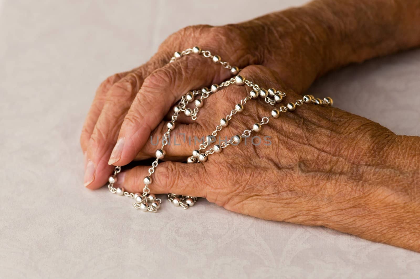 macro of elderly caucasian hands holding a silver rosary