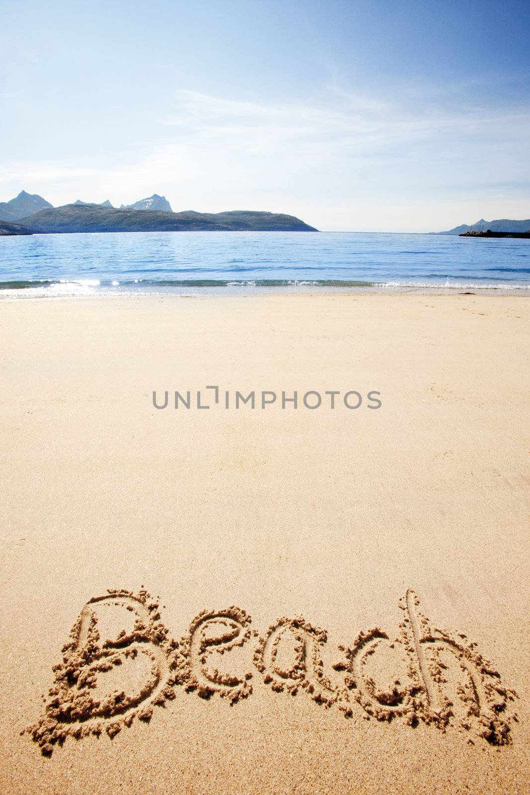 Beach written in the sand on the coast with mountains in the background