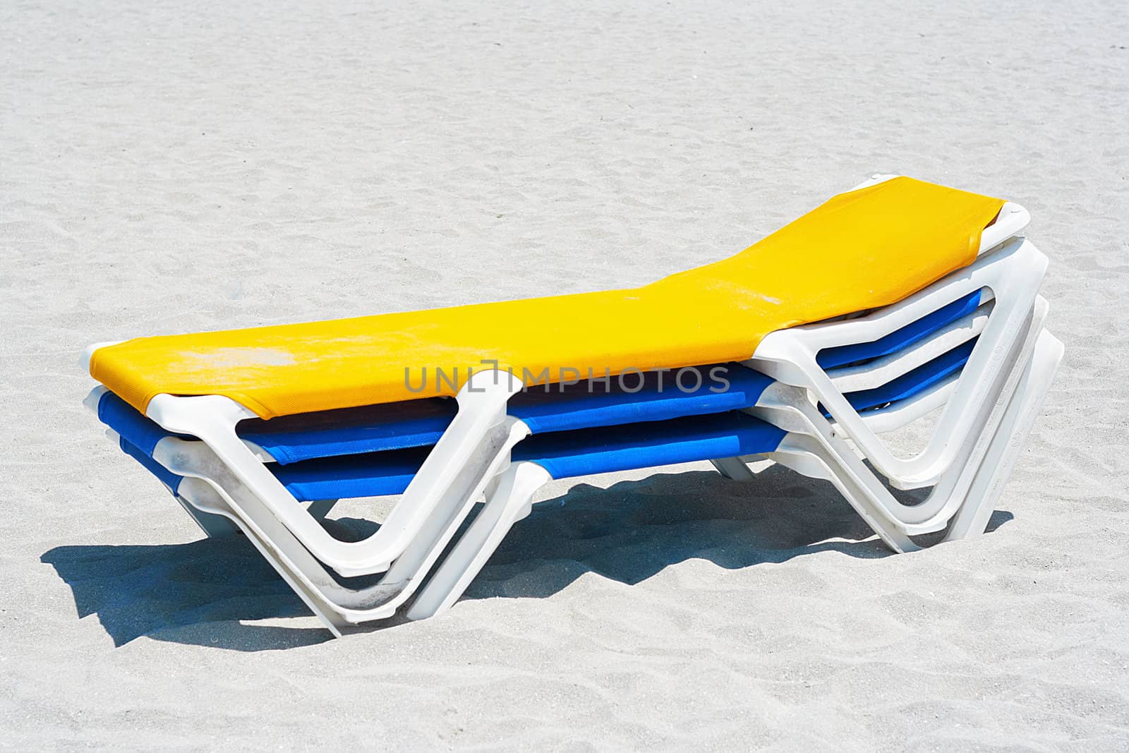 A stack of yellow and blue beach chairs in the sand