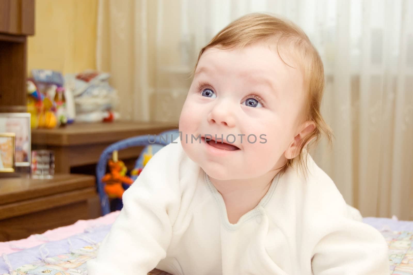 Blue-eyed baby boy lying on bed and smiling