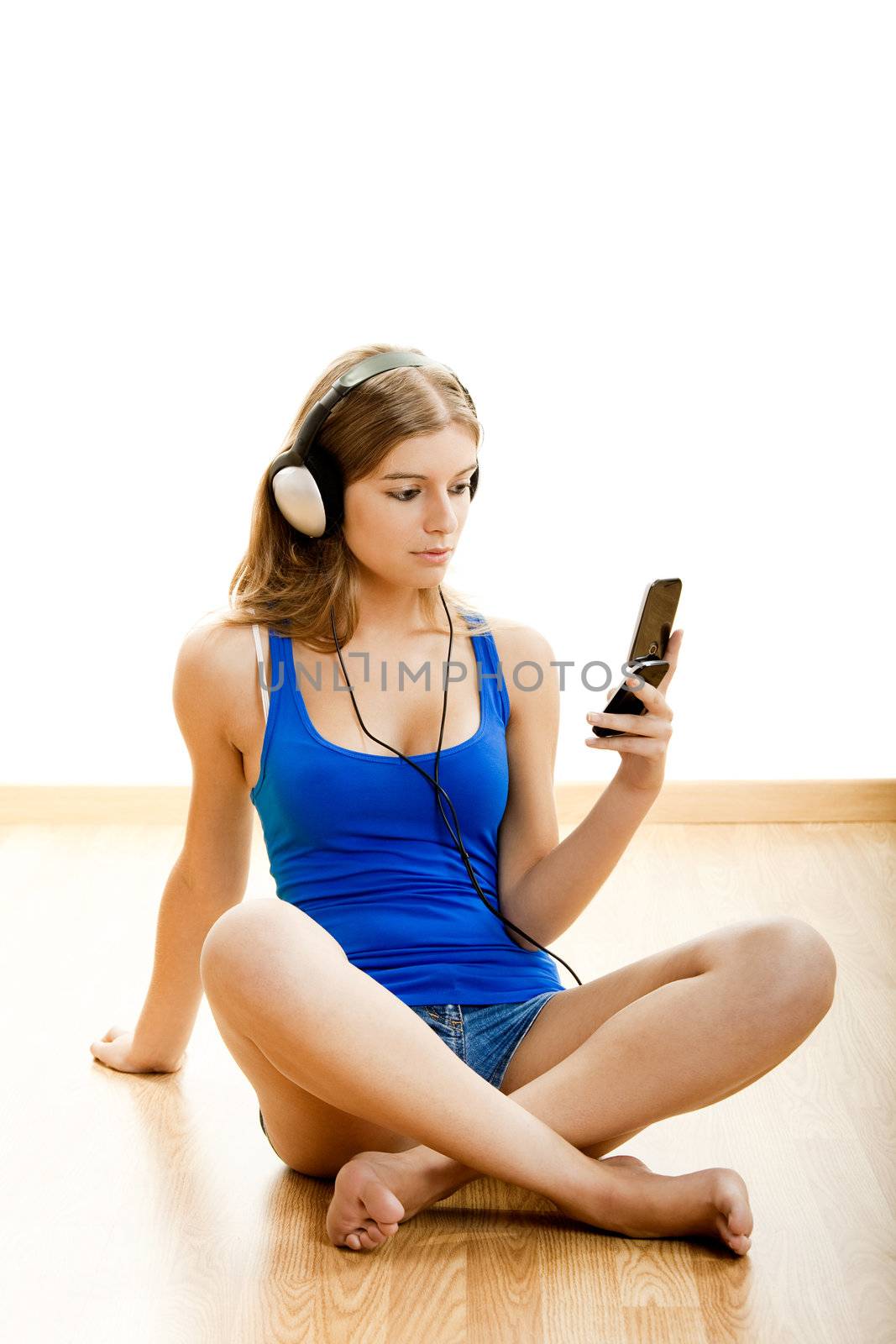 Beautiful young woman sitting on floor with headphones and holding a celphone