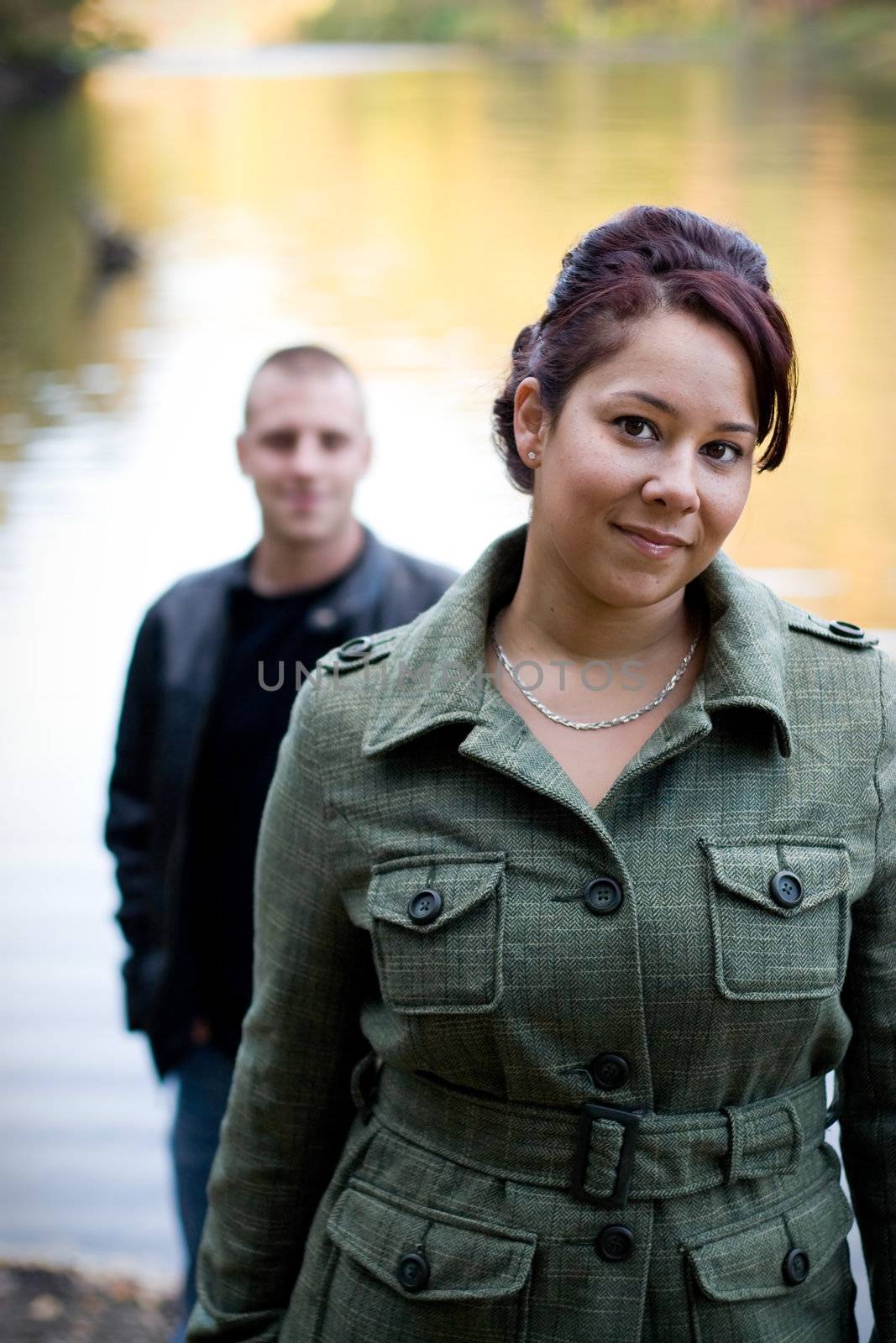 A young happy couple standing by a lake in autumn.  Shallow depth of field with focus on the woman.