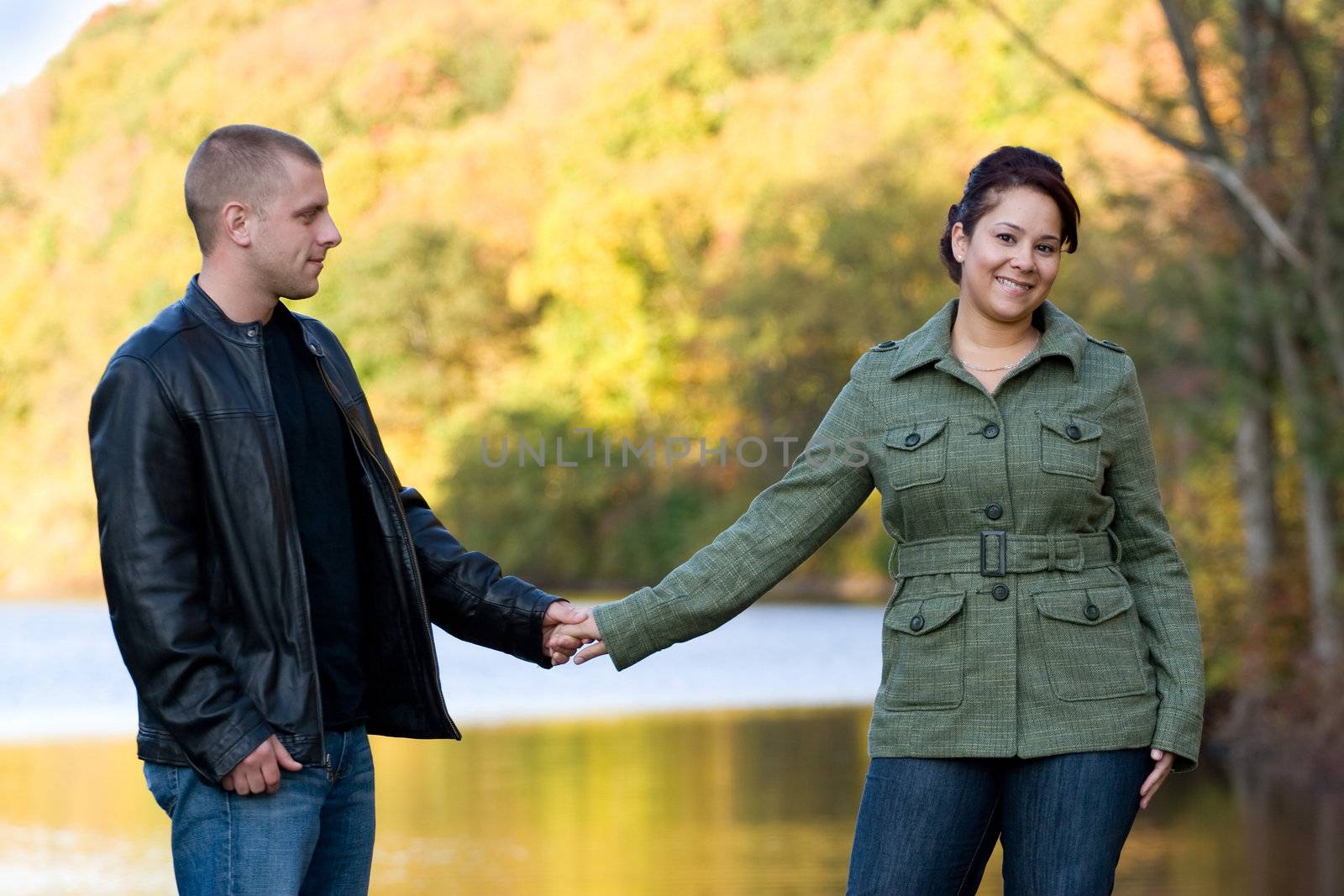 A young happy couple outdoors by a lake in autumn.