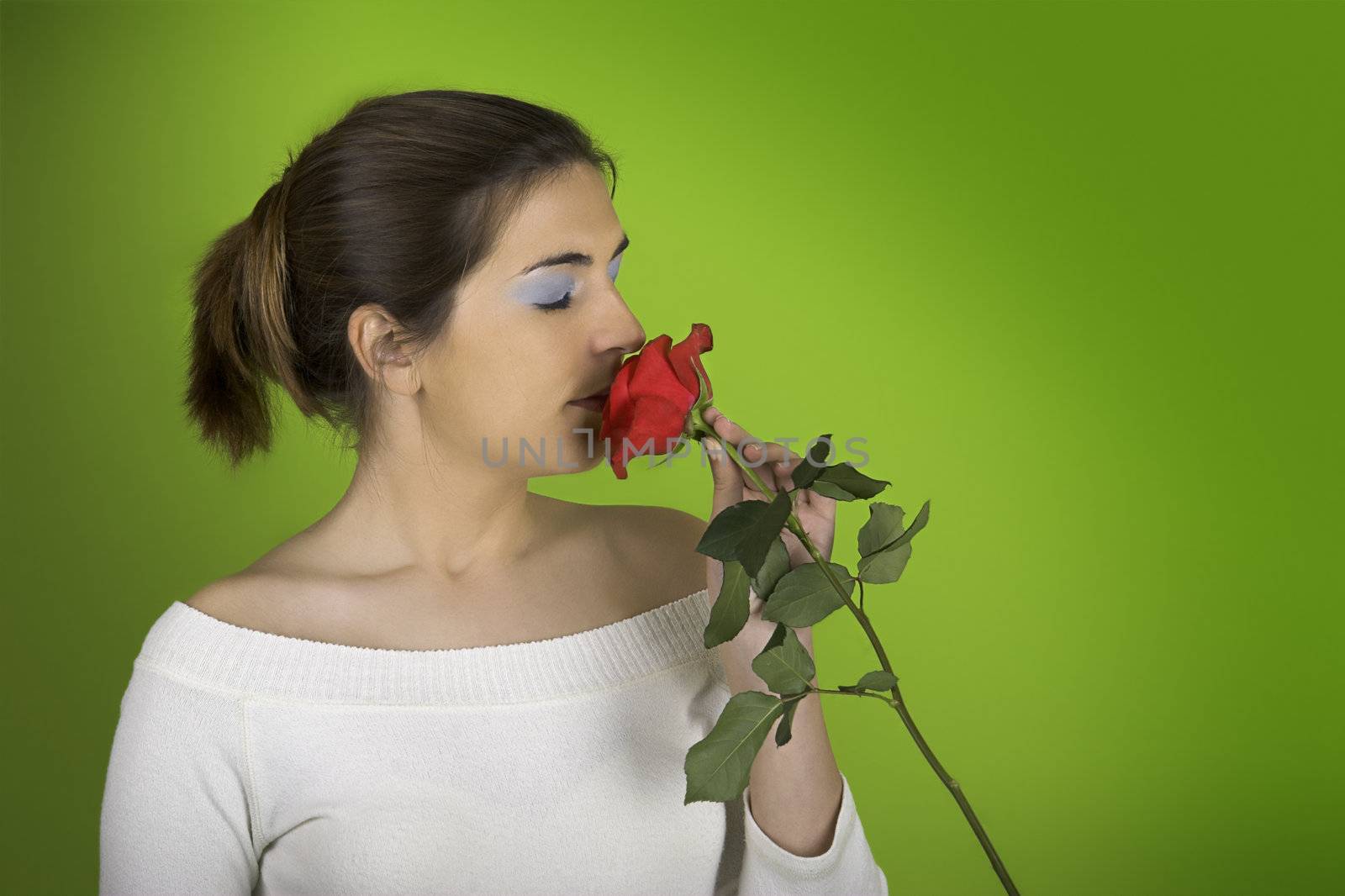 Portrait of a beautiful woman smelling a red rose on a green background