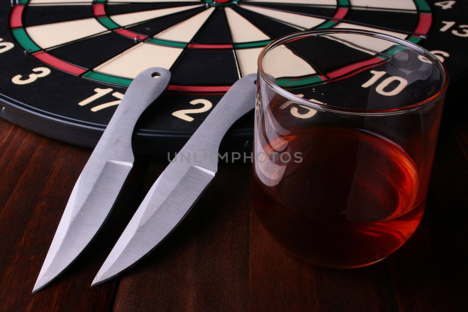 Two knifes for a throwing, a target and a glass of whisky.