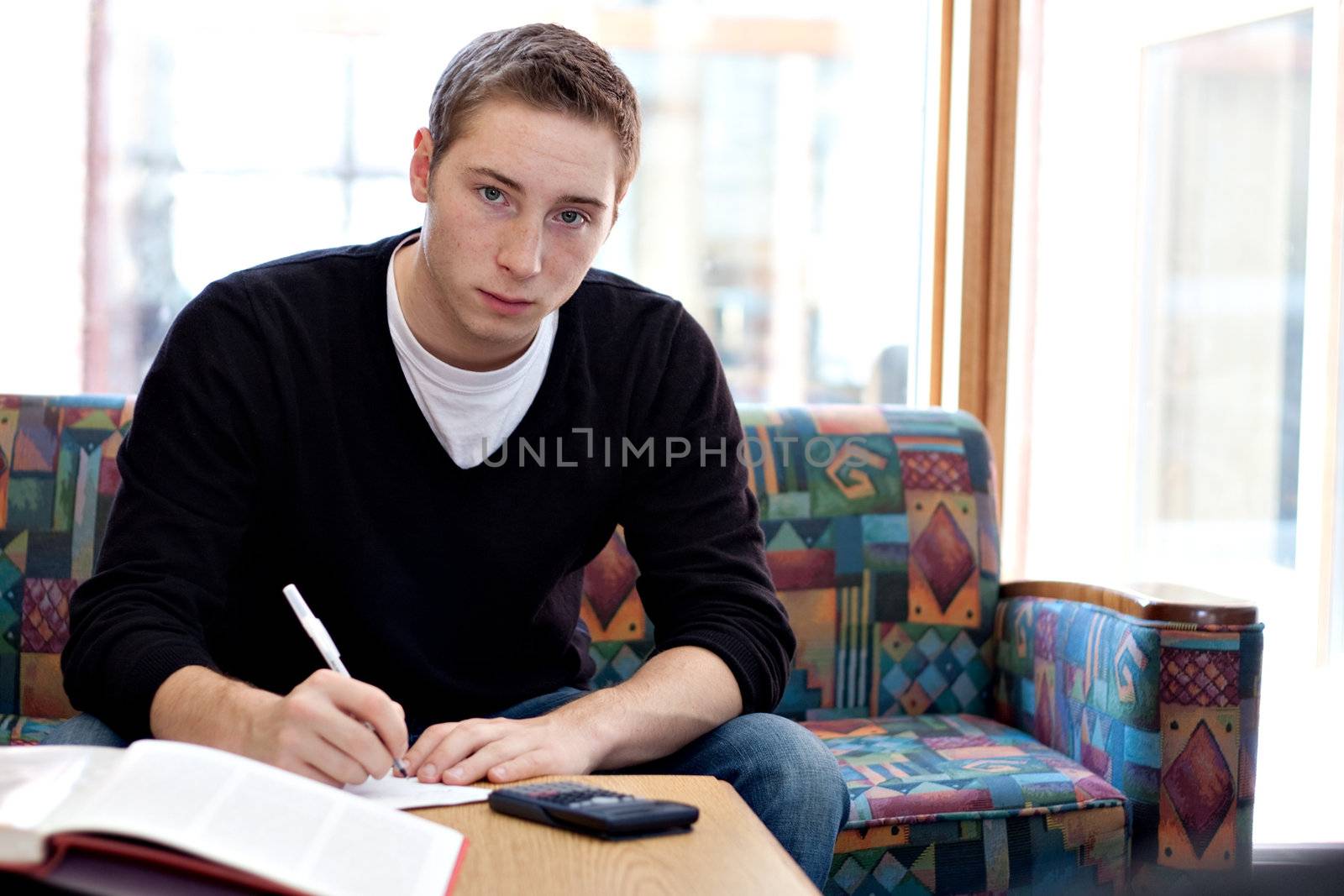 A young man working on his science physics or math homework in an educational setting.