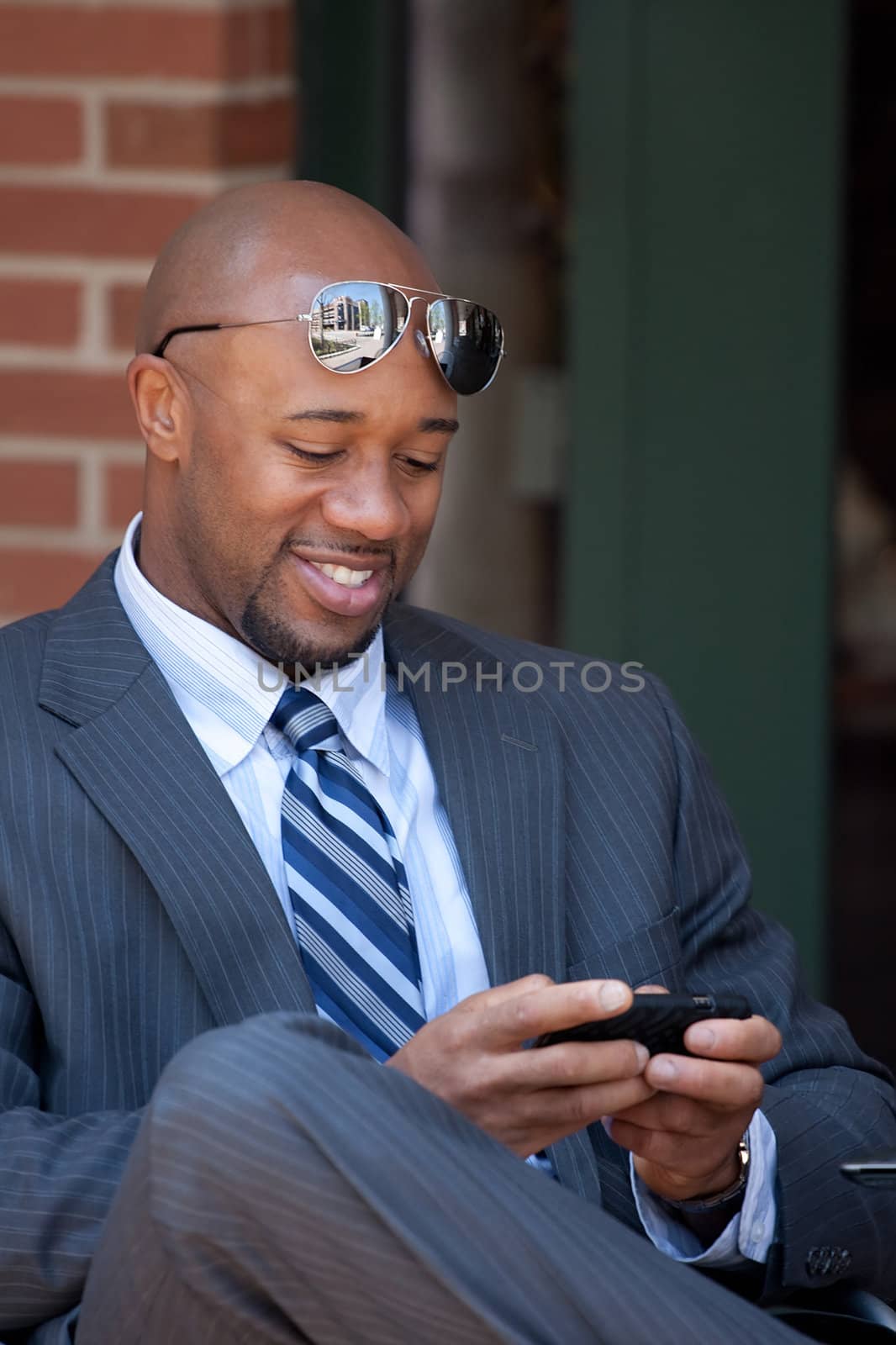 A good looking African American business man works on his smartphone with a smile on his face.