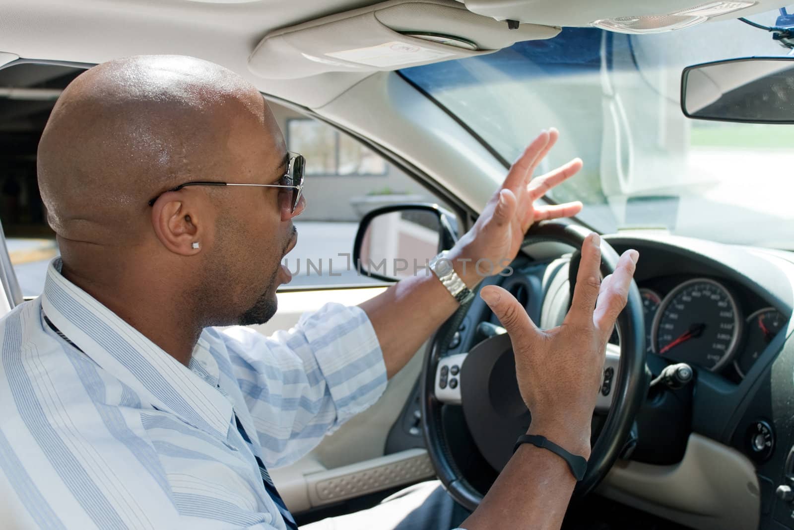 An irritated business man driving a car is expressing his road rage with his hands in the air.