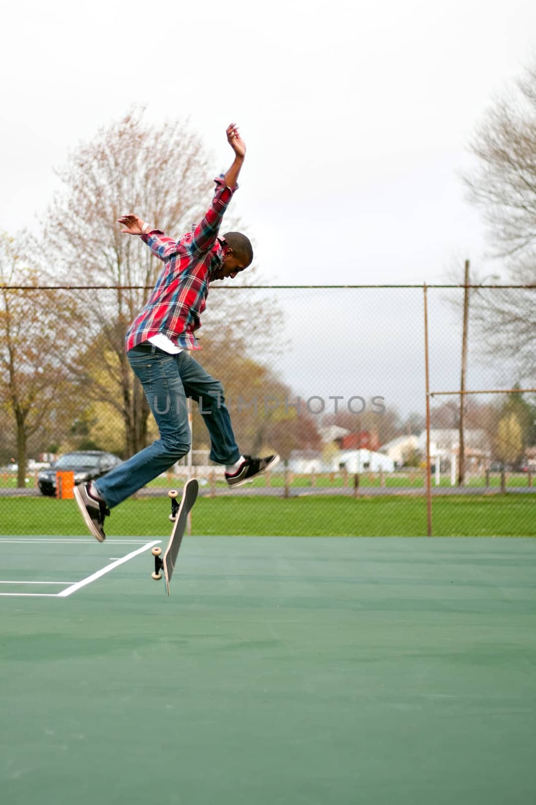 A skateboarder performing jumps or ollies on some tennis courts.  Slight motion blur showing the movement on the arms and legs.