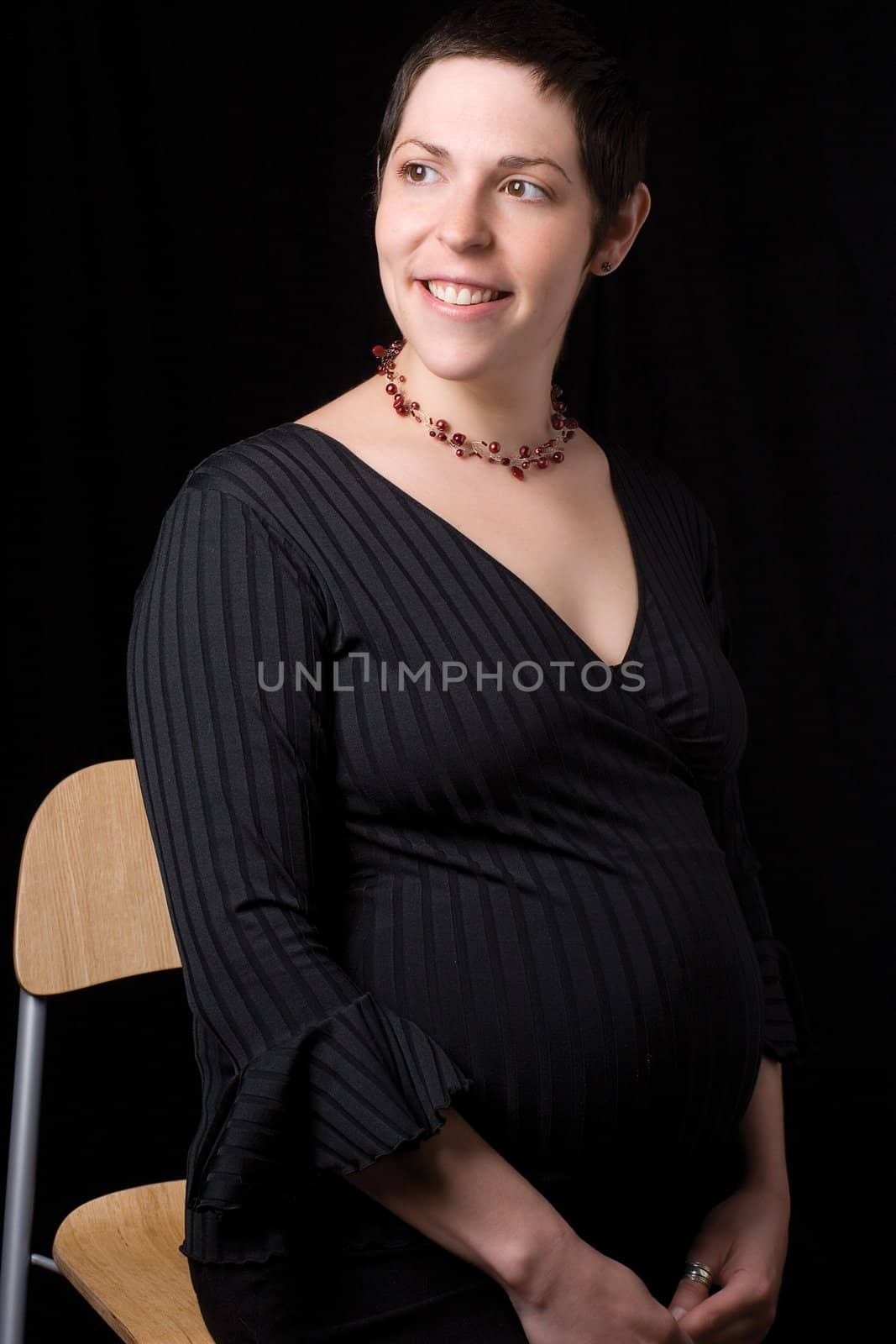 Sitting portrait of a late twenty pregnant women looking to the far left with great big smile