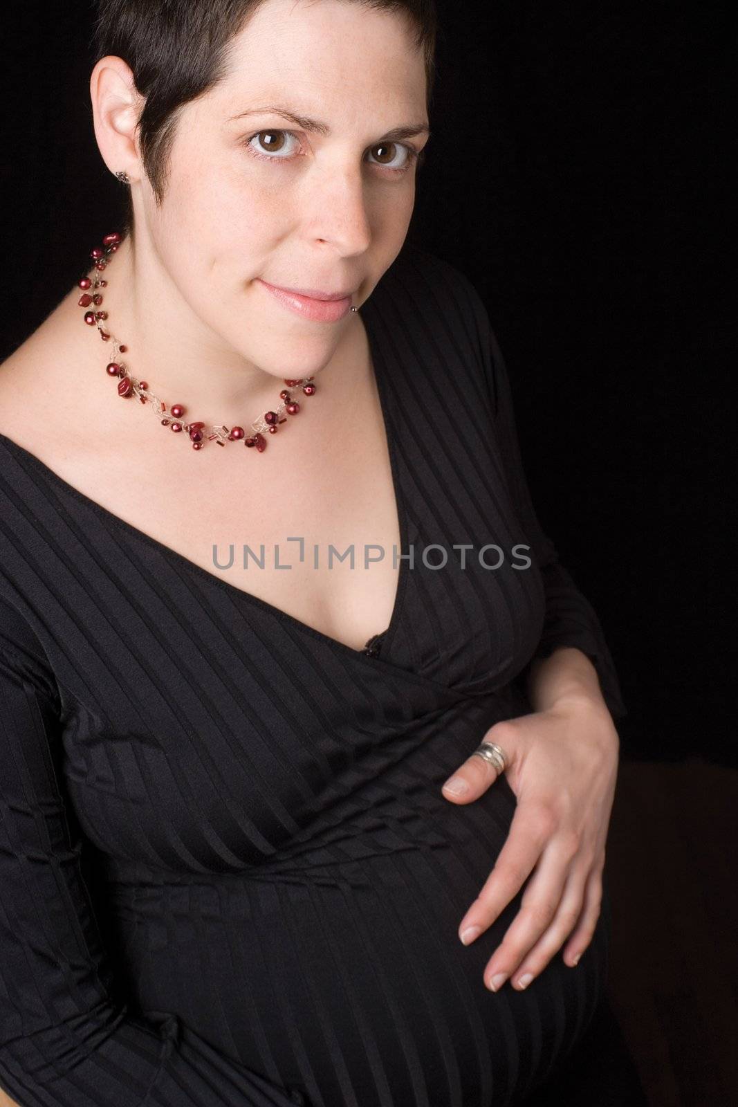 Sitting portrait of a late twenty pregnant women with shy, holding her belly. looking at the camera