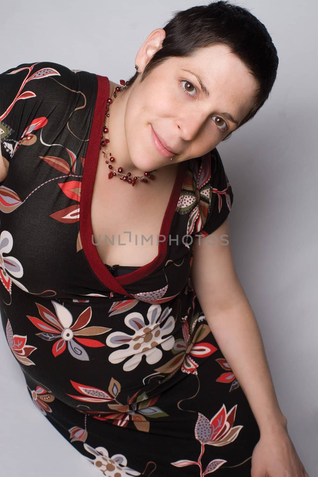 Late twentie pregnant woment sitting on a white background with a great big smile