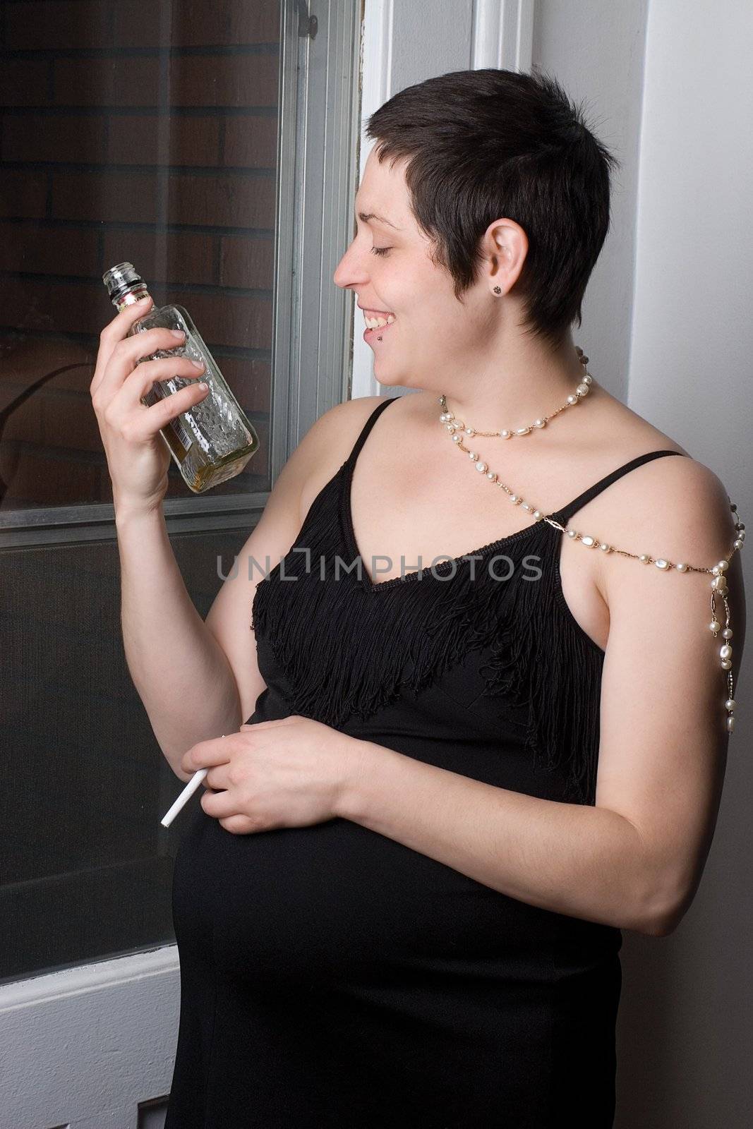 Late twentie pregnant woman in old fashion evening dress with a bottle of alchool in one hand and a unlite cigarette in the other