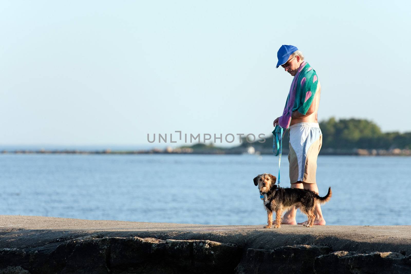 A middle aged man walks a cute borkie beagle yorkie mix puppy at the beach.