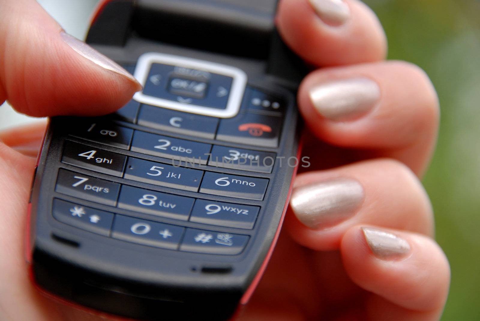 Female hand holding mobile phone keypad / green background