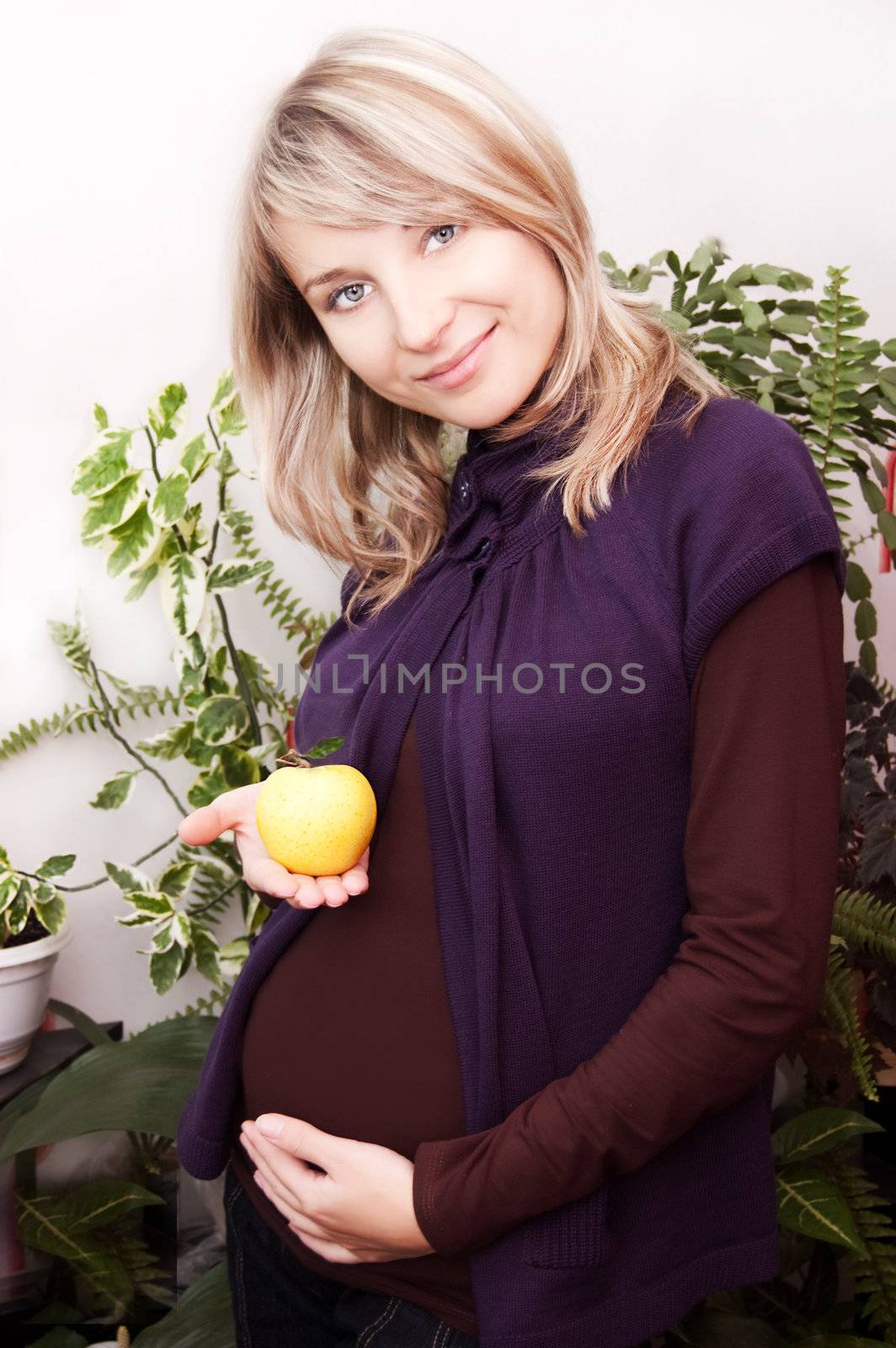 Smiling pregnant woman with yellow apple over home plants