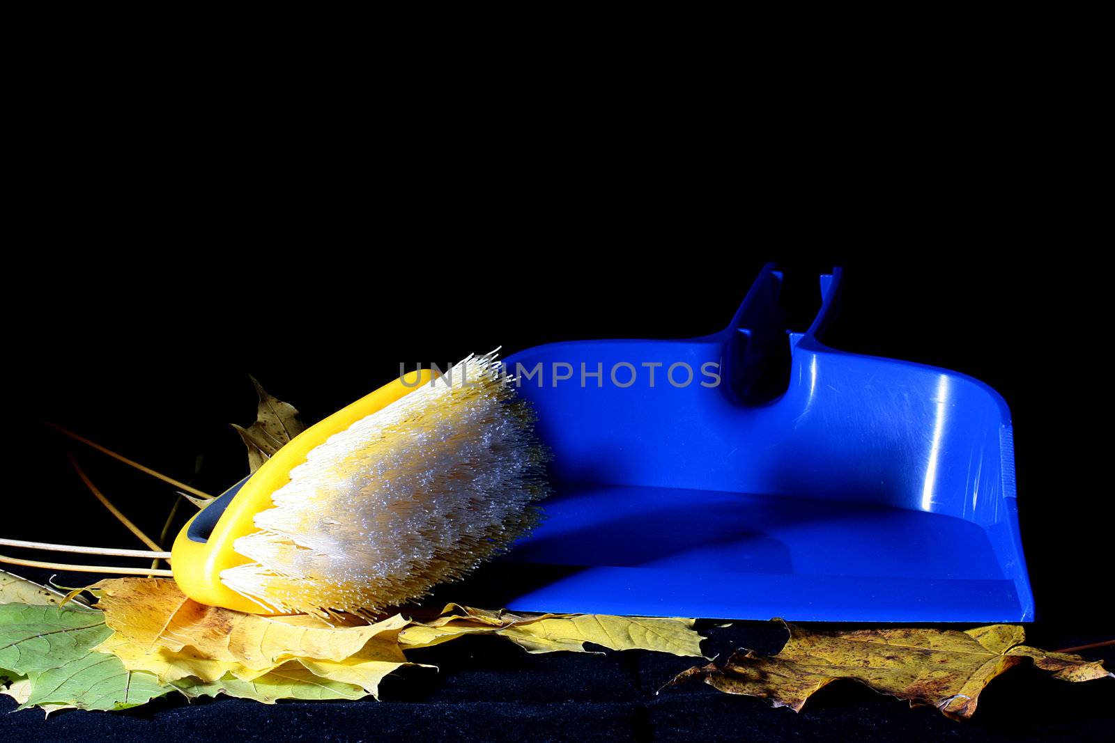 Brush for dust and a dustpan on autumn yellow leaves, a background - black.