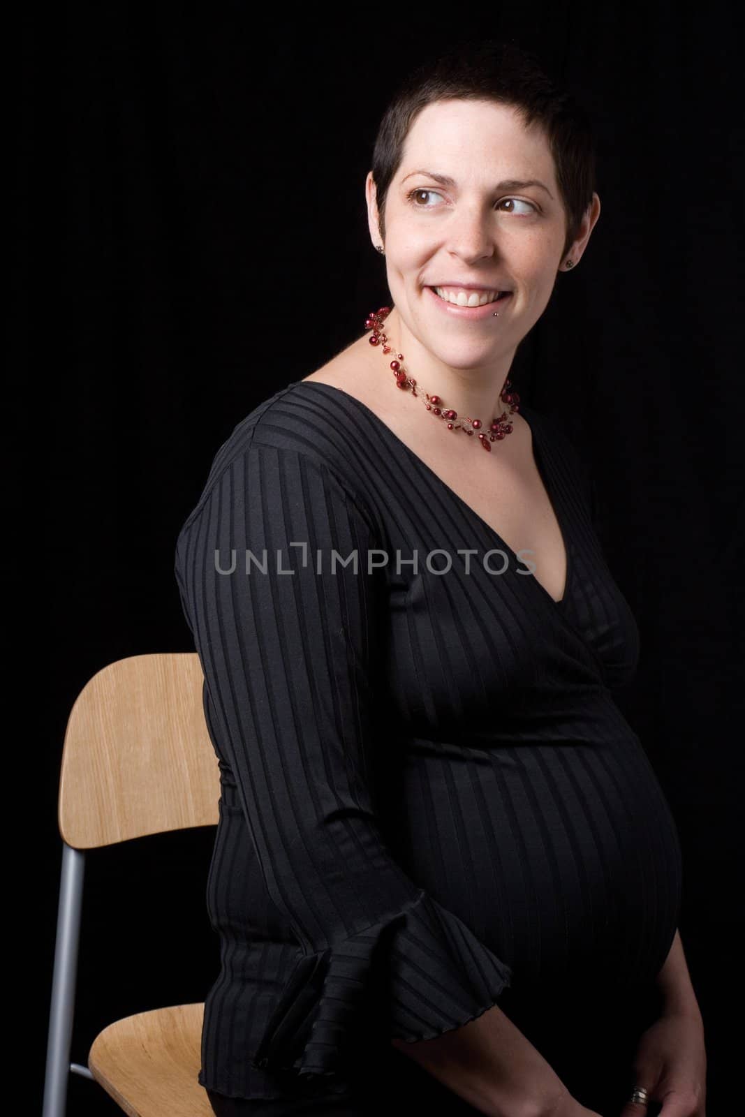 Sitting portrait of a late twenty pregnant women with a great big smile looking to the far right