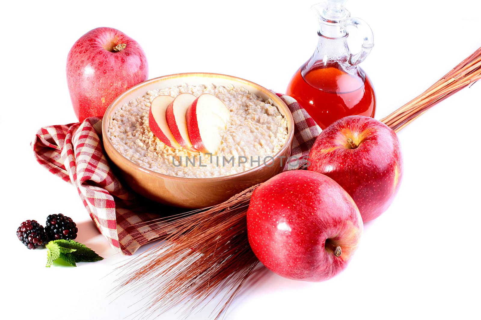 Porridge with apples, ears and berries, on a background a bottle with oil and a towel.