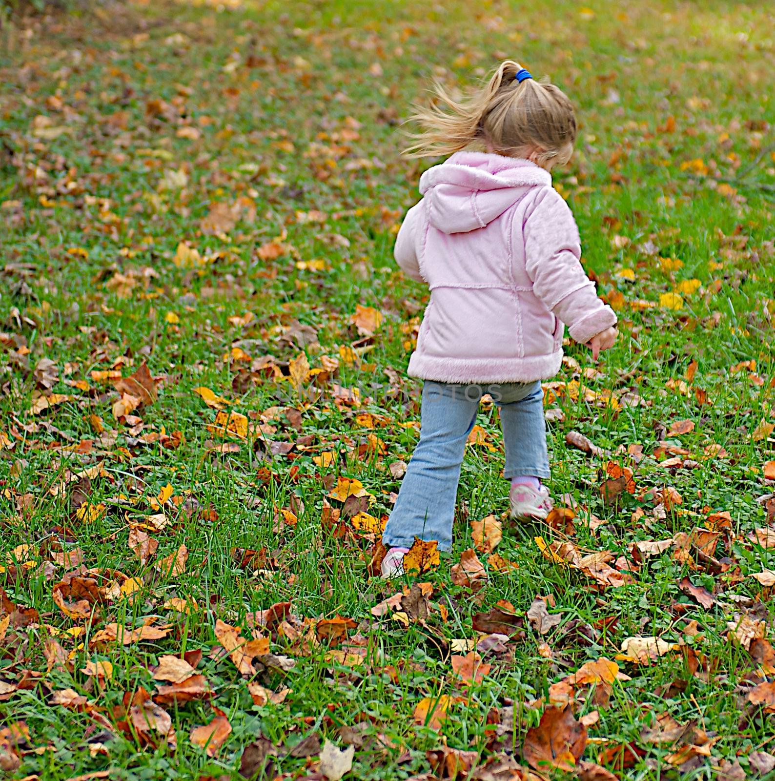 Cute young girl skipping in the autumn leaves of a playground.