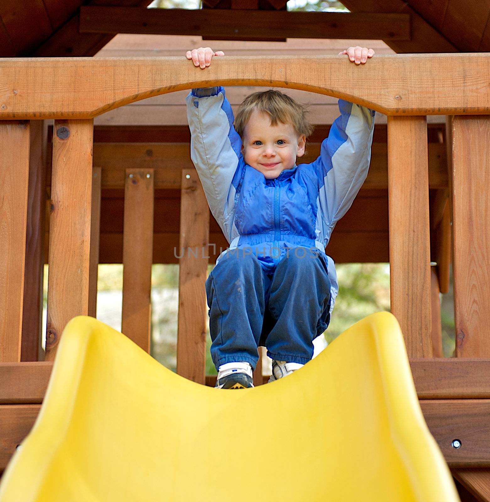 Cute young boy grasping the bar while getting ready to slide down a sliding board at the playground.