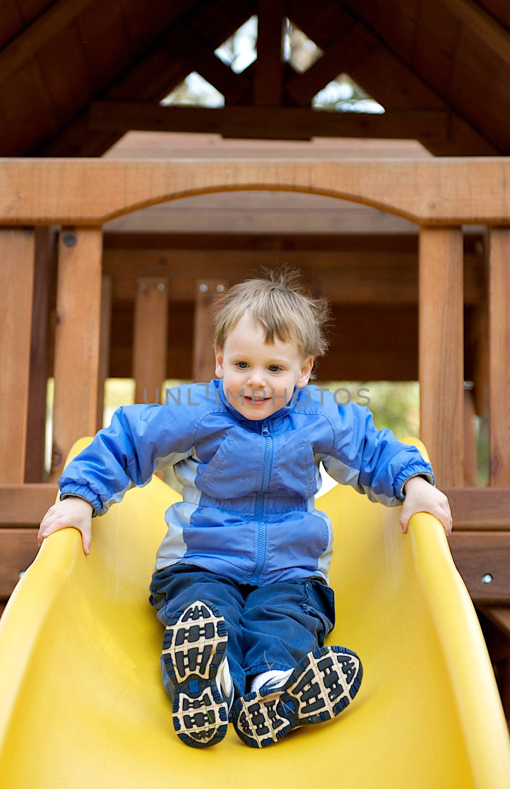 Young boy smiling while sliding down a sliding board in a playground.