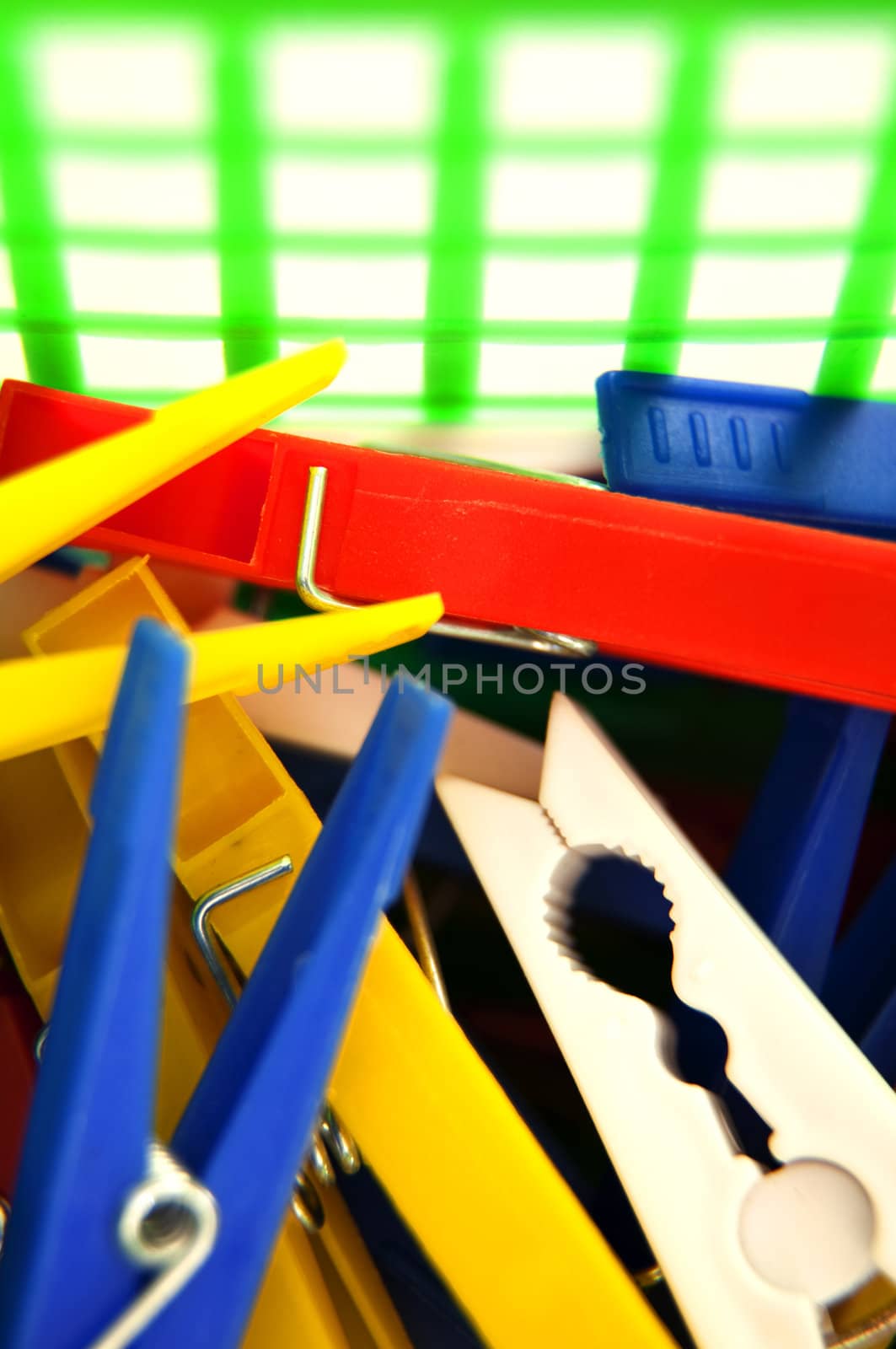 close up of colourful plastic pegs in a green peg basket