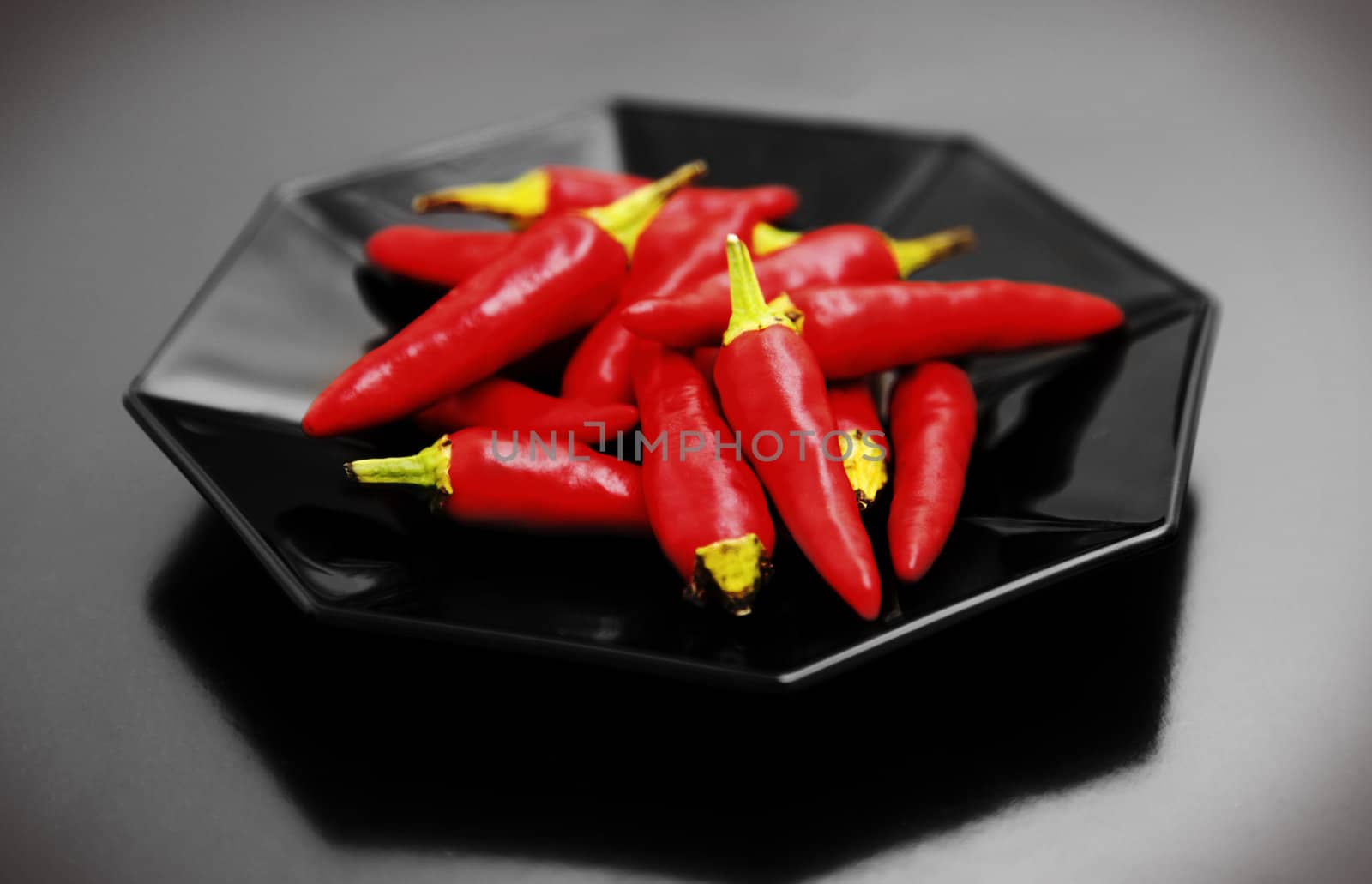 Small pile of red chiilies on a, octagonal black plate.