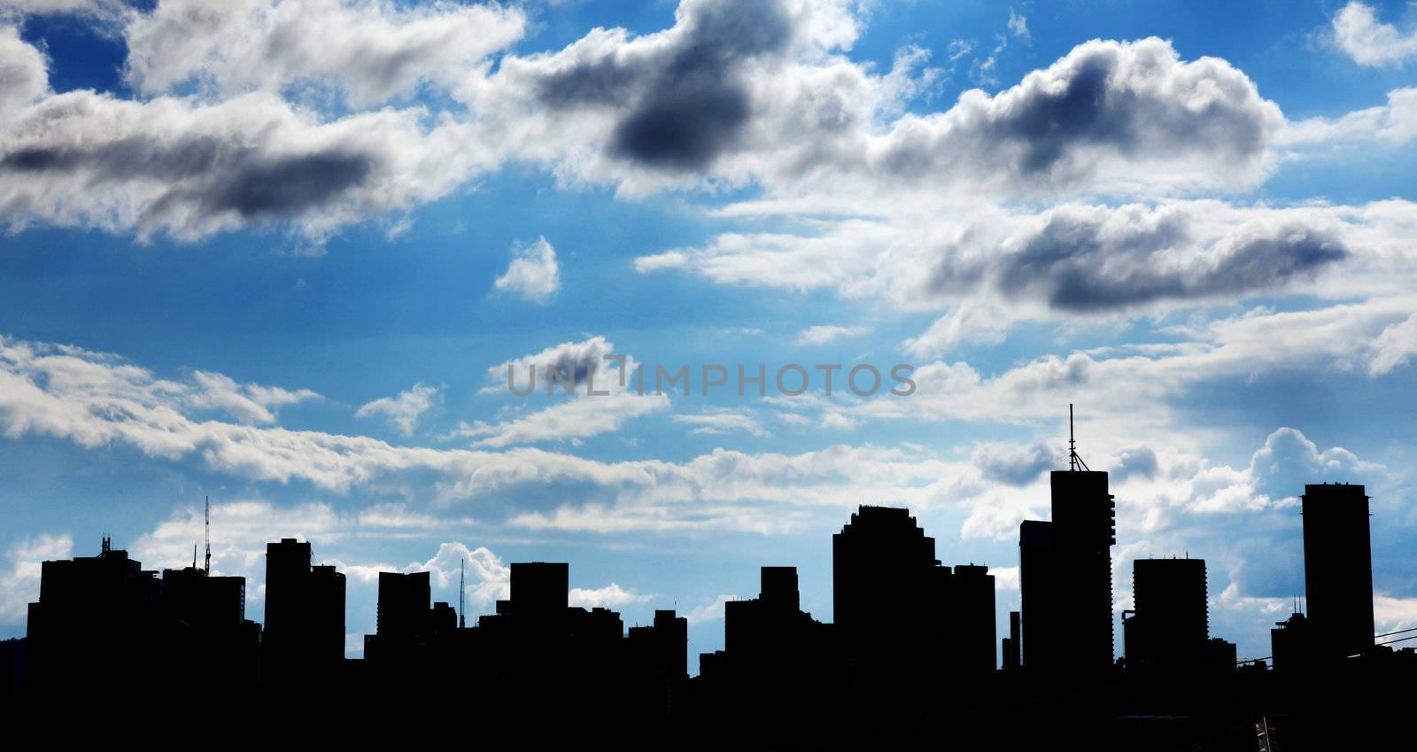 Silhouette of a cityscape against a cloudy blue sky