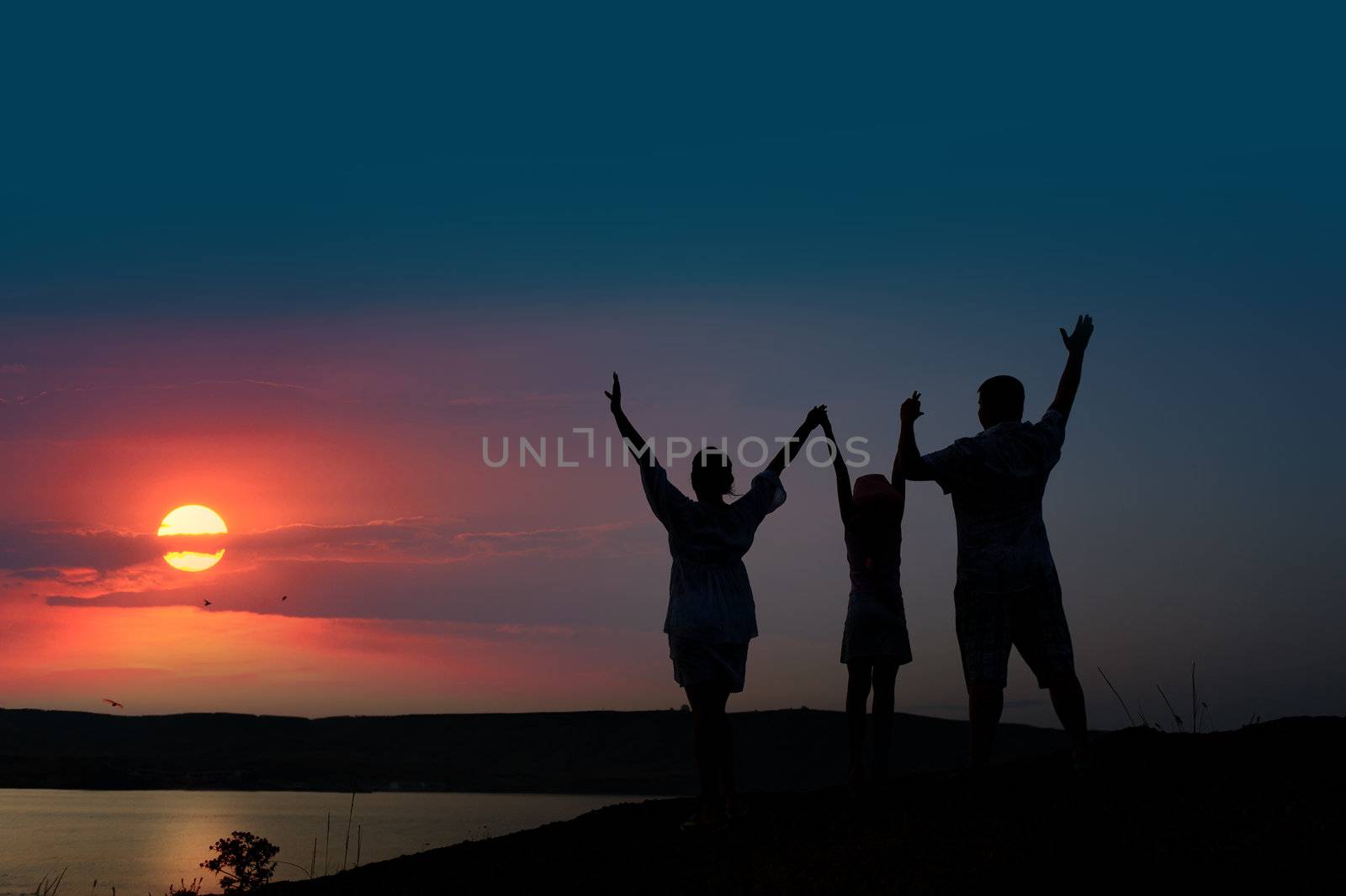 The family from three persons welcomes the sunset sun.