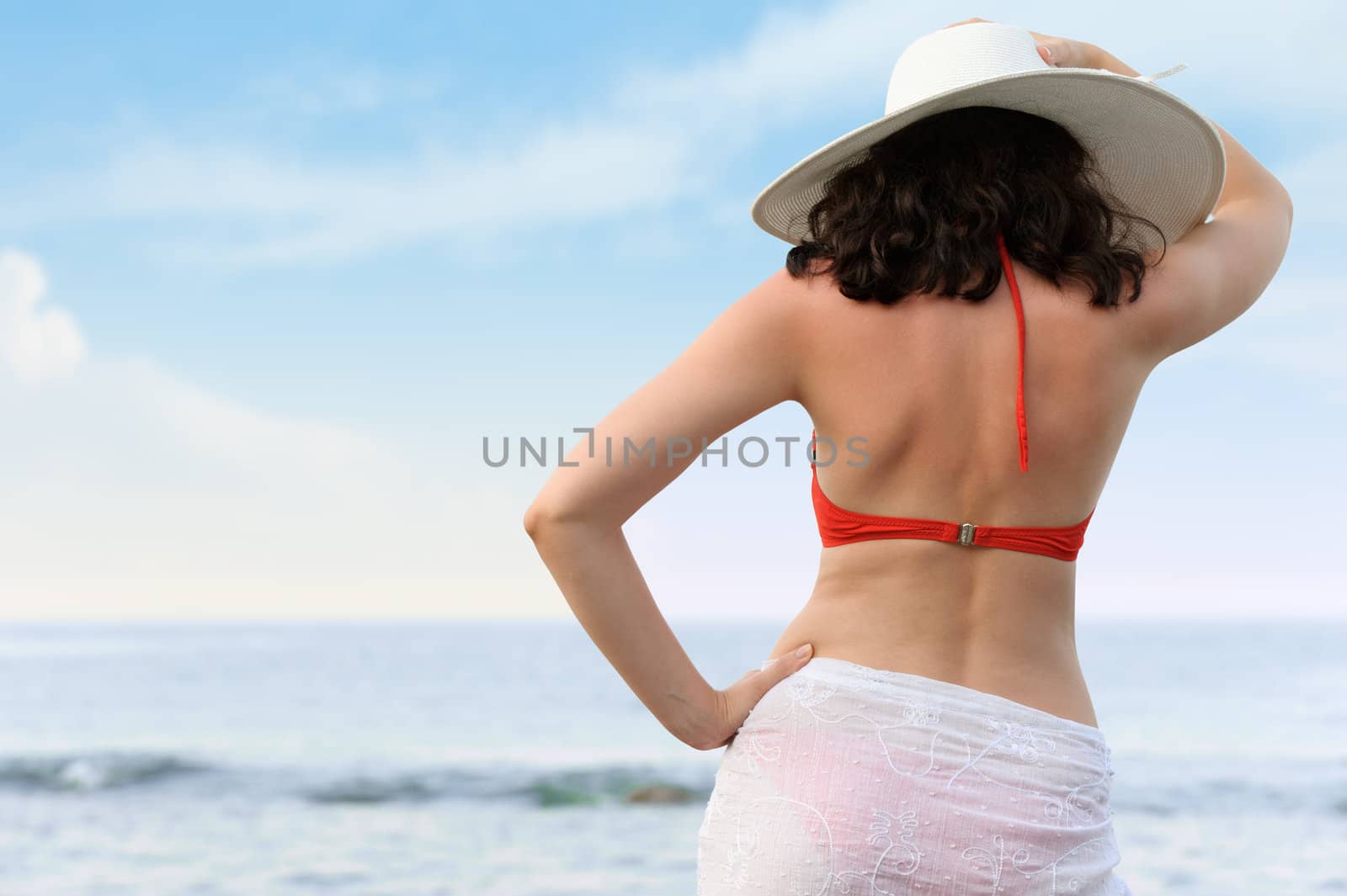 The woman on sea coast in a hat. The rear view