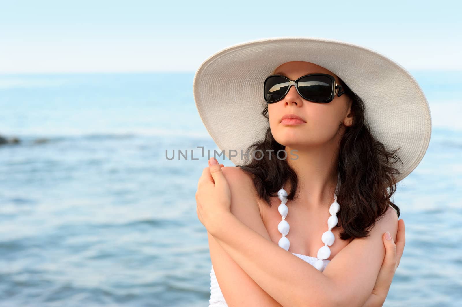 The woman on seacoast. In sun glasses, a sundress, a hat.