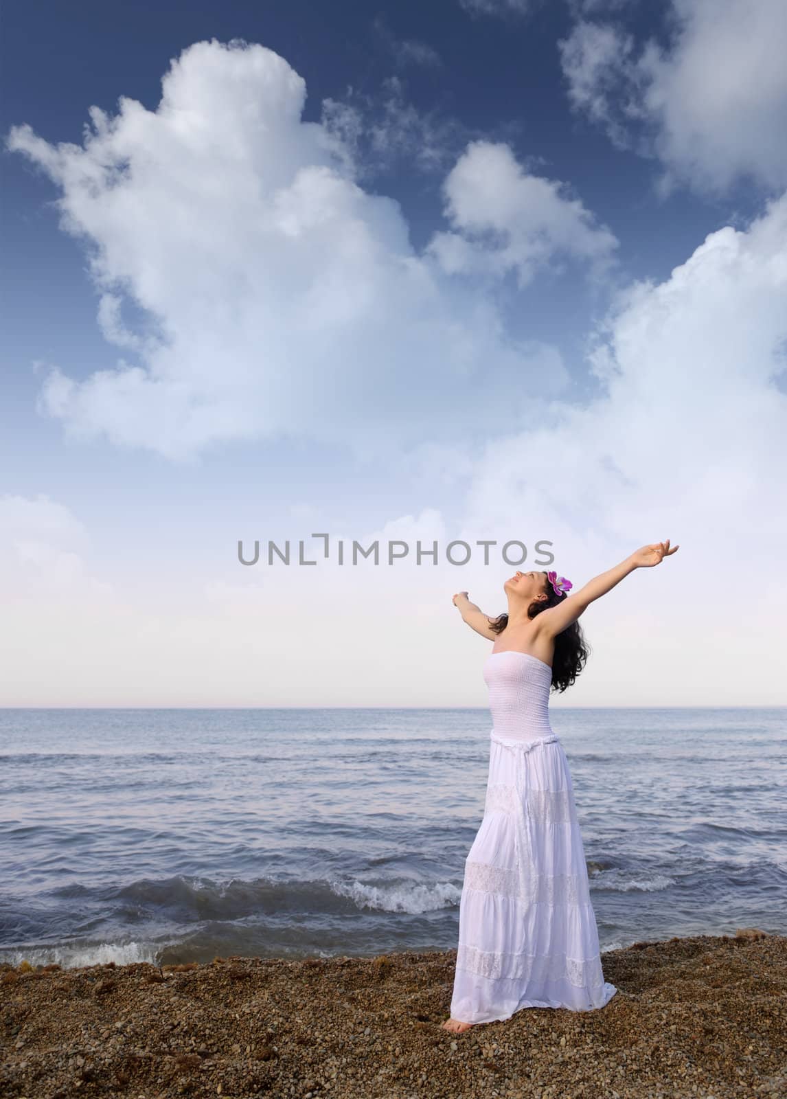 The woman in a white sundress on seacoast with open hands. Cloud sky