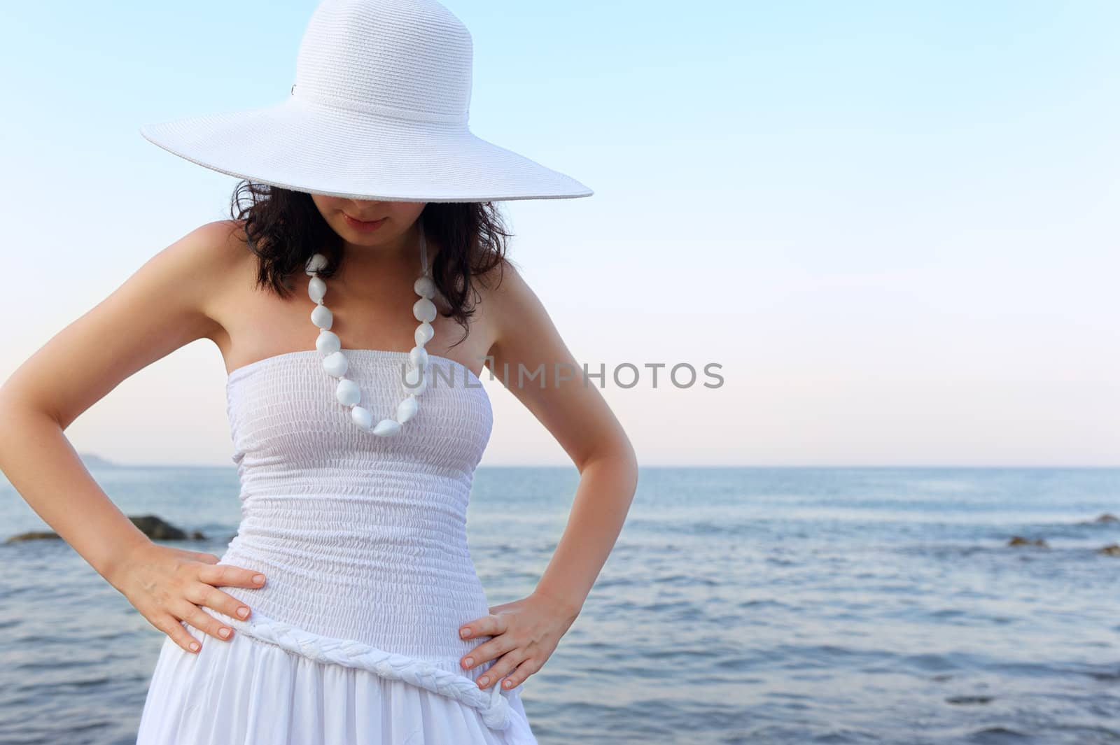 The woman on seacoast. In sun glasses, a sundress, a hat.